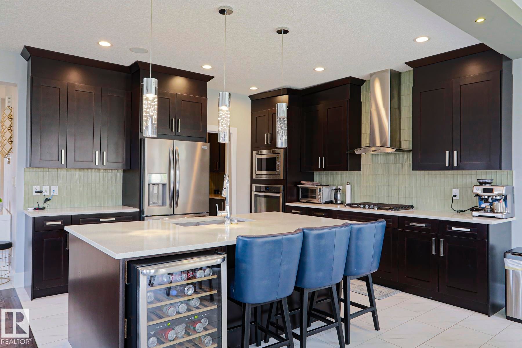 Spacious kitchen featuring dark wood cabinetry, light-toned countertops, and a full suite of stainless steel appliances - 1304 Ainslie Wynd Sw, Edmonton, AB - Indoor Photo Showing Kitchen With Stainless Steel Kitchen With Upgraded Kitchen
