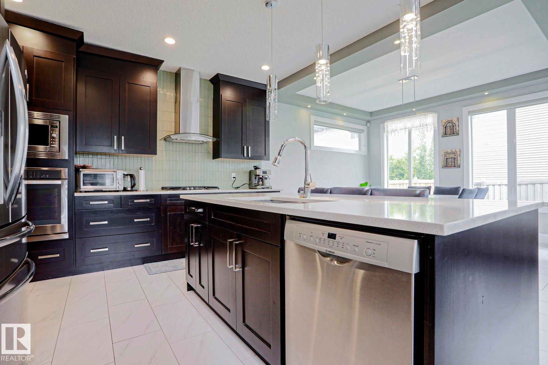 Contemporary kitchen featuring dark wood cabinetry and a large center island with a white countertop - 1304 Ainslie Wynd Sw, Edmonton, AB - Indoor Photo Showing Kitchen With Upgraded Kitchen