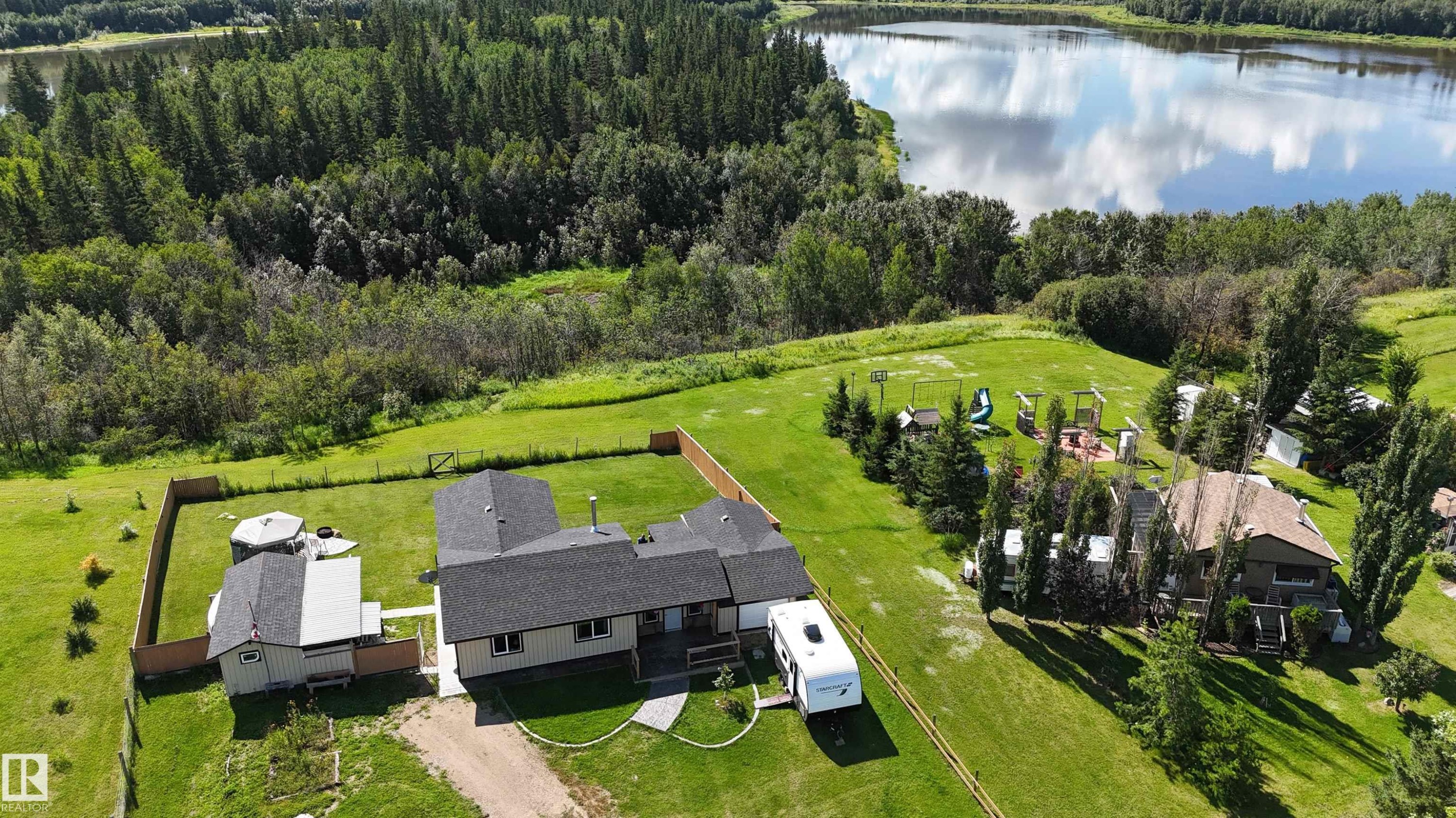 Spacious exterior with light-colored siding, dark trim, a covered porch, an expansive lawn, and a wooden fence - 315 57201 Rng Rd 102, Rural St. Paul County, AB