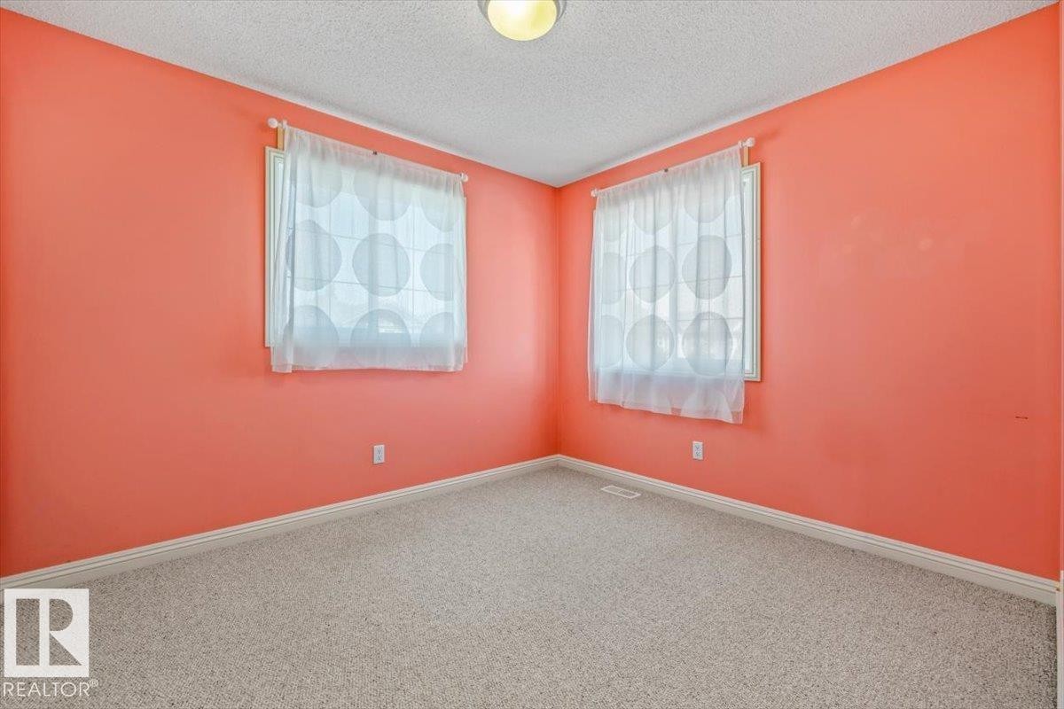 Room featuring two windows with sheer privacy treatments, coral-painted walls, light-colored carpeting, and a ceiling-mounted light fixture - 2407 Hagen Way, Edmonton, AB