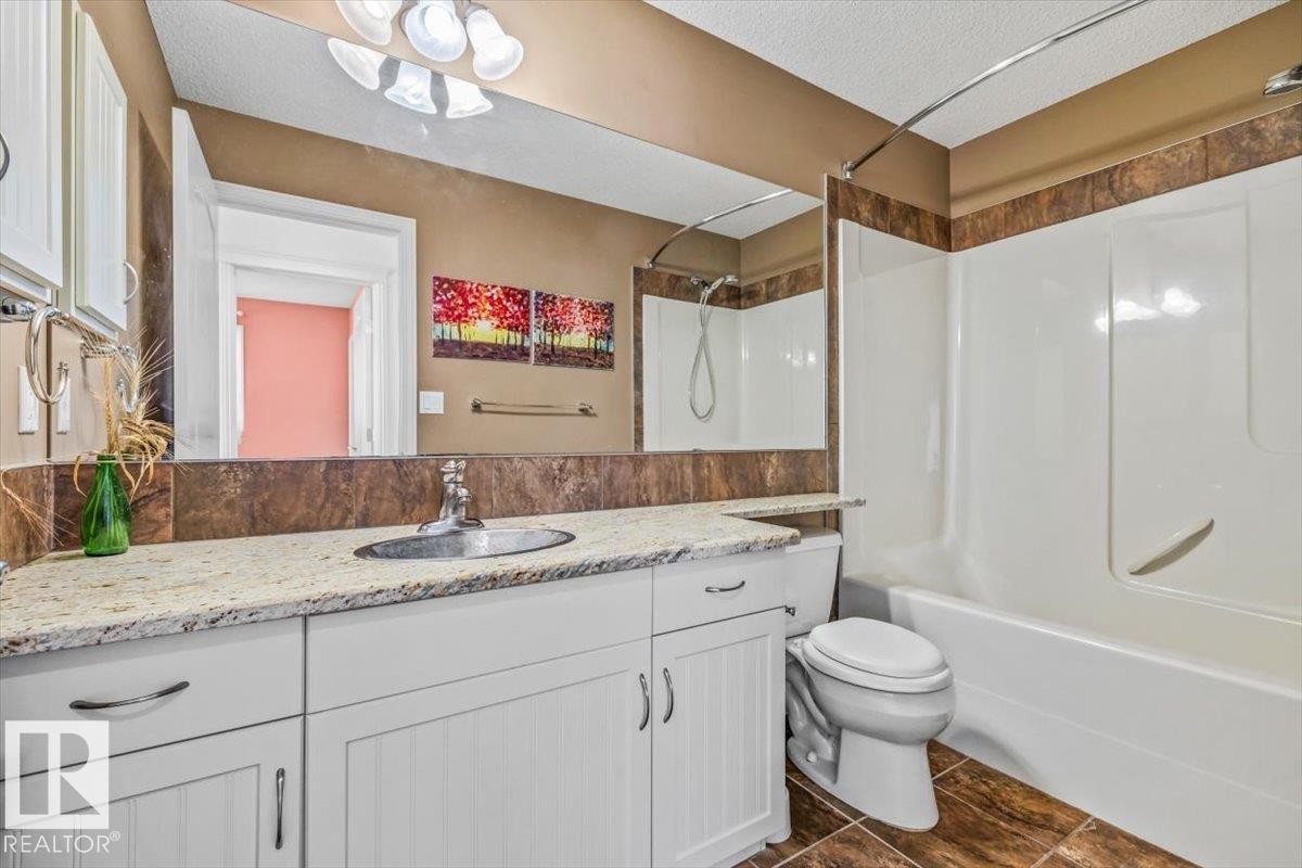 Bathroom featuring a white vanity with a light-toned countertop, a large wall-mounted mirror, a shower-tub combination, and tiled flooring - 2407 Hagen Way, Edmonton, AB