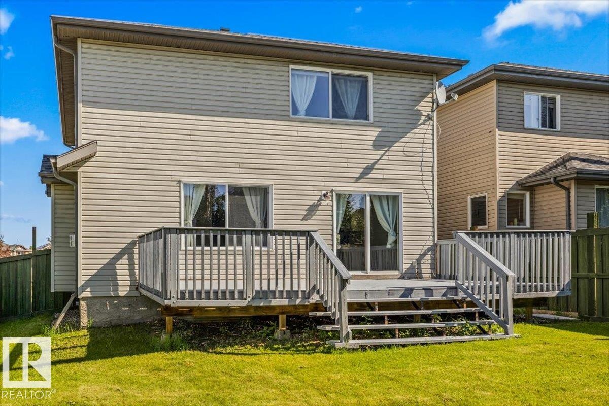 Rear exterior featuring a wooden deck with stairs, a sliding glass door, and a grass lawn - 2407 Hagen Way, Edmonton, AB