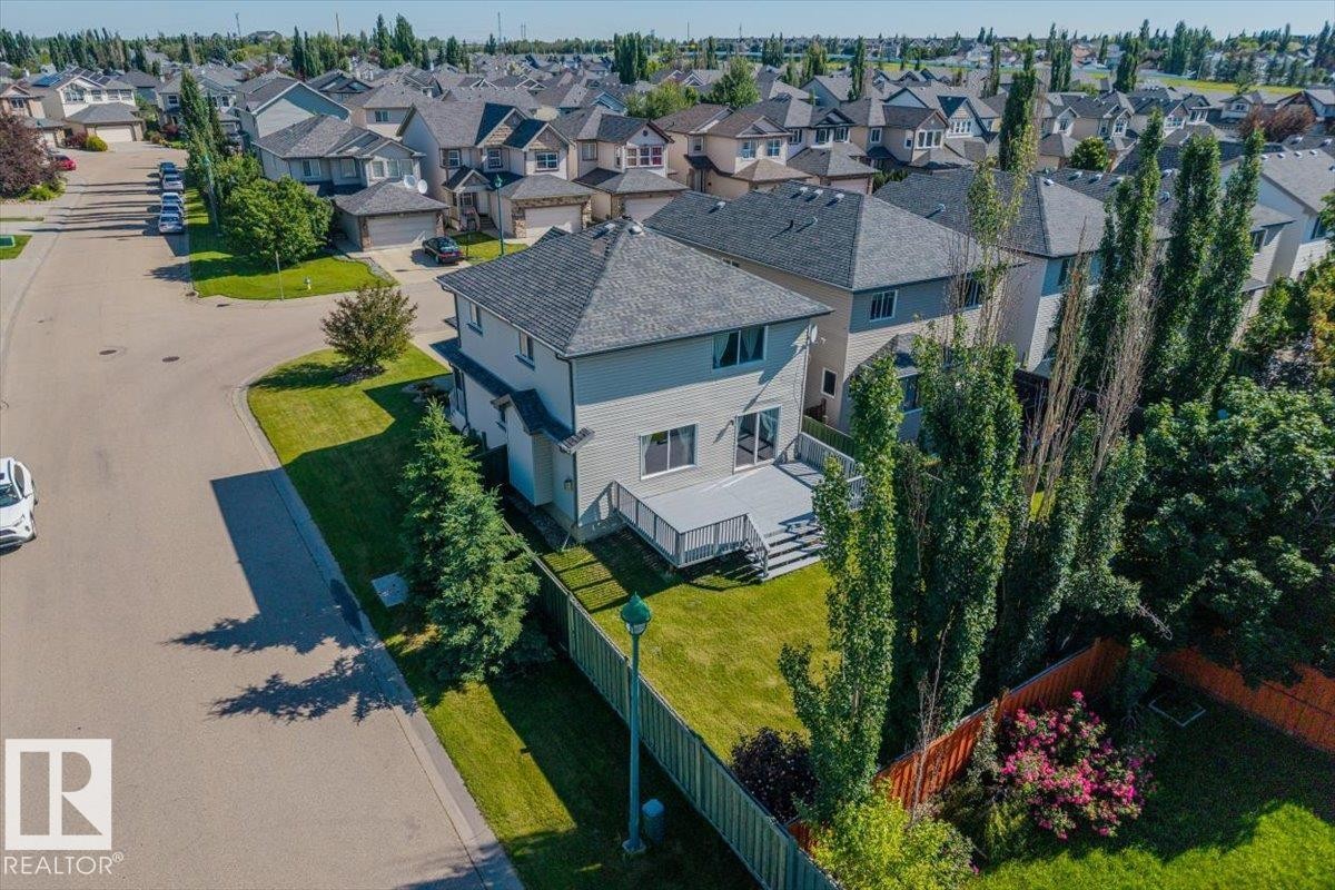 Two-story residence with a multi-level composite deck overlooking a fenced backyard with mature trees - 2407 Hagen Way, Edmonton, AB