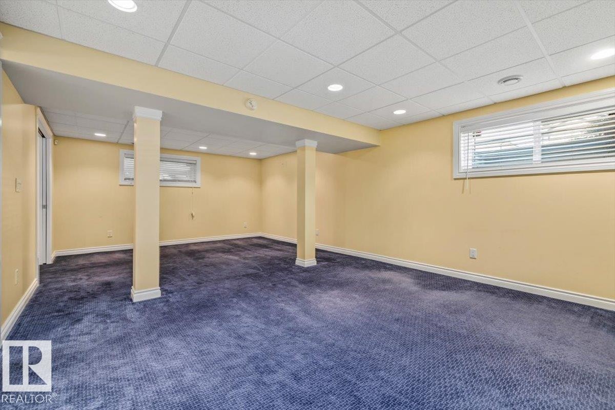 Spacious room featuring blue carpet flooring, light yellow walls, and a white grid ceiling with recessed lighting - 2407 Hagen Way, Edmonton, AB