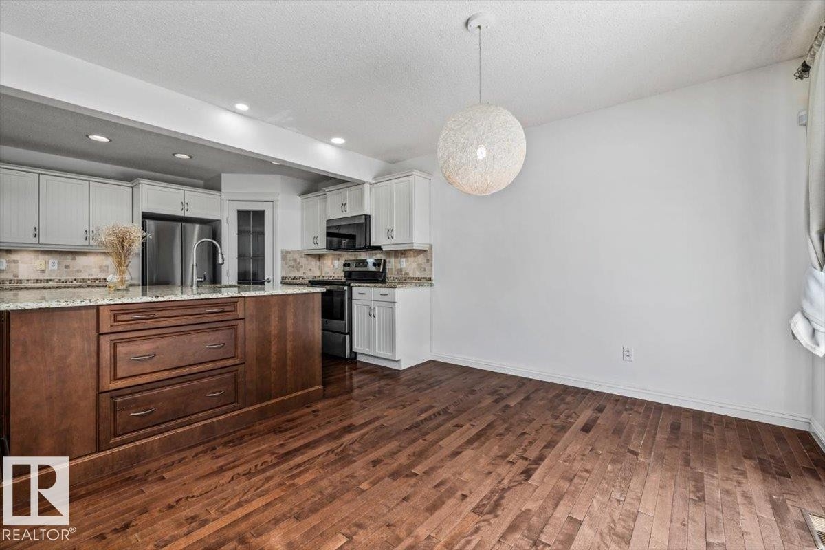 Gourmet kitchen and dining area featuring a two-toned island with ample storage, stainless steel appliances, recessed lighting, and wood-finish flooring - 2407 Hagen Way, Edmonton, AB