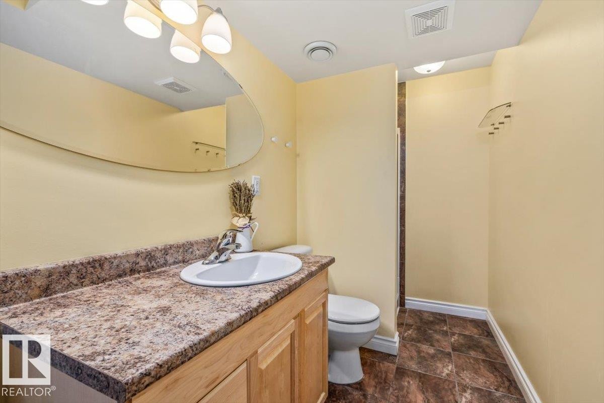 Bathroom featuring a light wood-finish vanity with an integrated sink, a patterned countertop, and a large wall-mounted mirror - 2407 Hagen Way, Edmonton, AB
