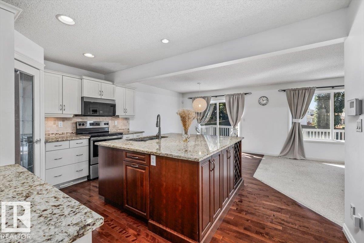 Open-concept kitchen featuring an oversized island with a wine rack, light-toned cabinetry, and granite countertops - 2407 Hagen Way, Edmonton, AB