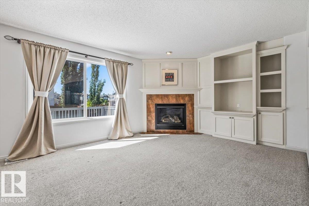 Corner fireplace with a stone surround and a traditional mantel, flanked by built-in cabinetry and shelving - 2407 Hagen Way, Edmonton, AB