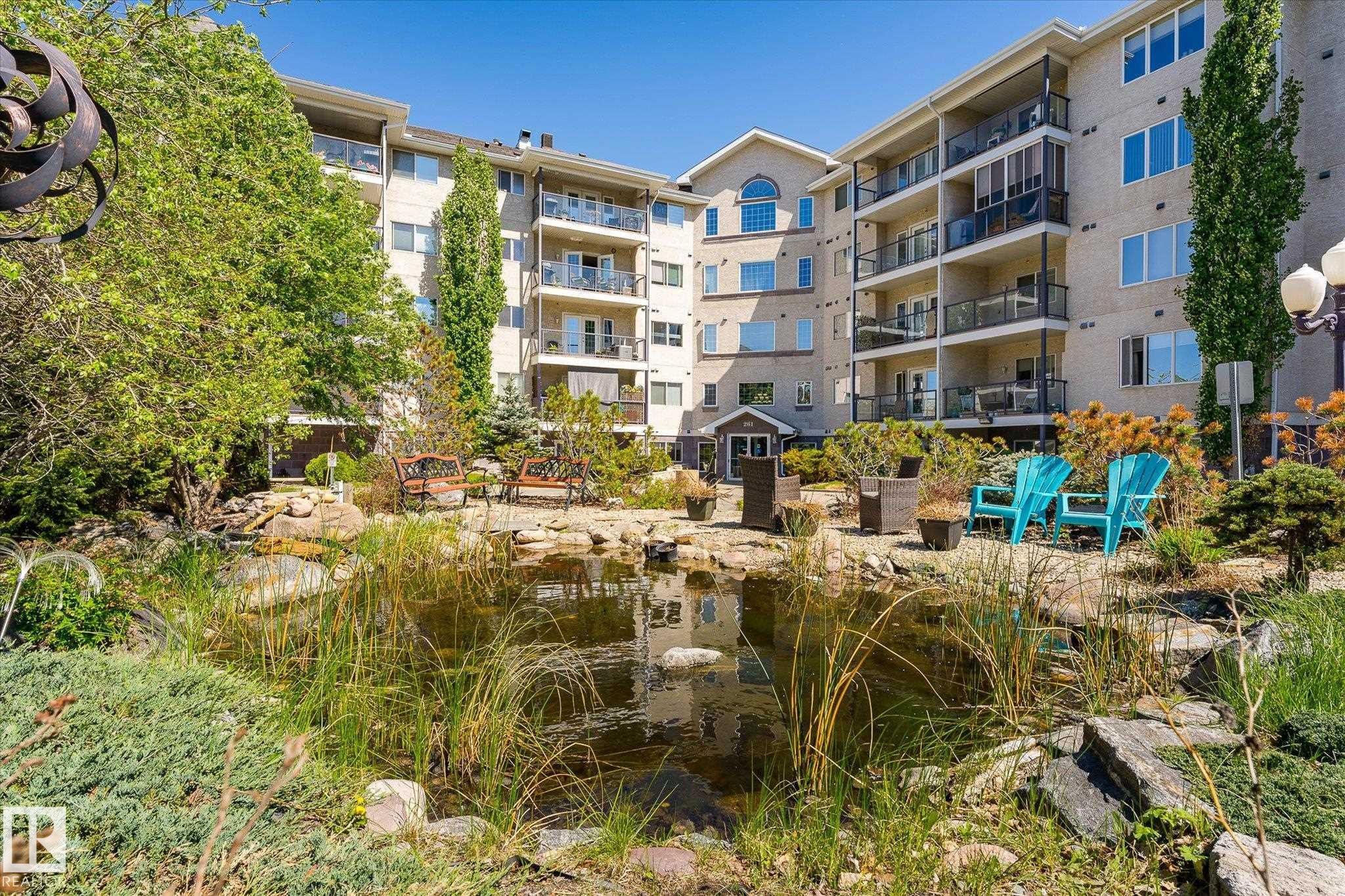 Landscaped courtyard featuring a tranquil pond with natural plantings, rock formations, and mature trees - #310 237 Youville Dr E Nw, Edmonton, AB - Outdoor With Balcony