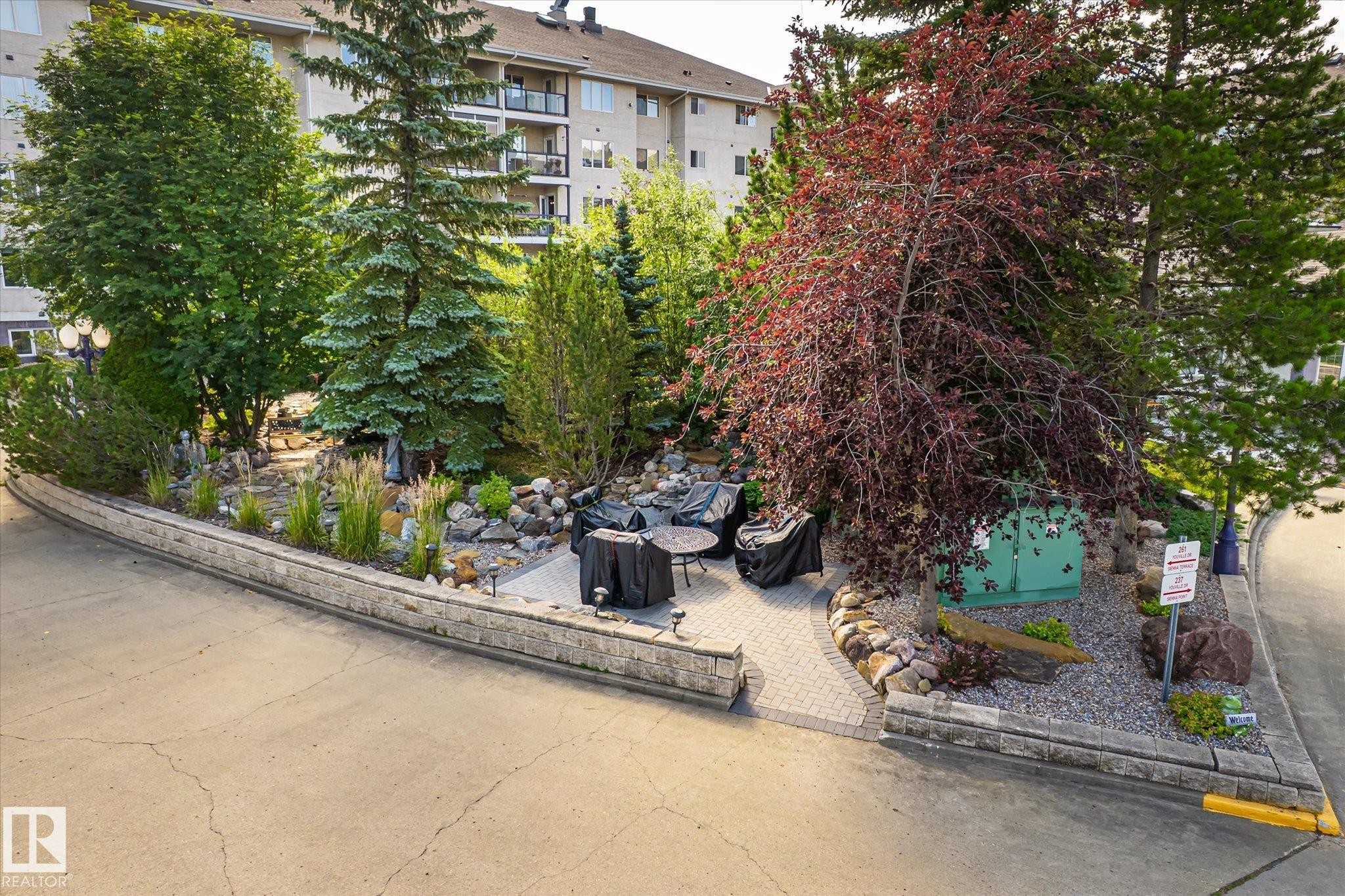Landscaped garden area featuring diverse mature trees and shrubs - #310 237 Youville Dr E Nw, Edmonton, AB - Outdoor With Balcony