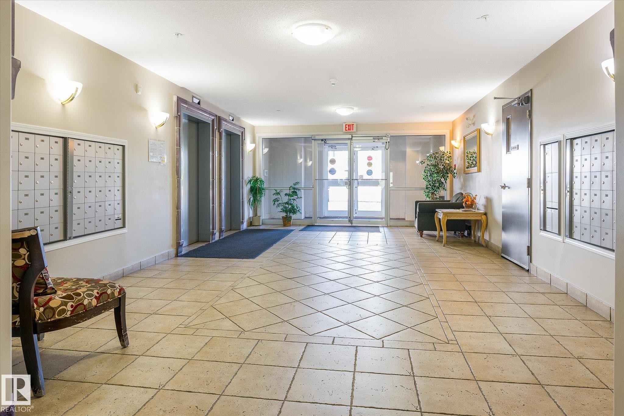 Spacious common area featuring patterned tile flooring, dual elevators, multiple wall sconces, and built-in mailboxes - #310 237 Youville Dr E Nw, Edmonton, AB - Indoor Photo Showing Other Room