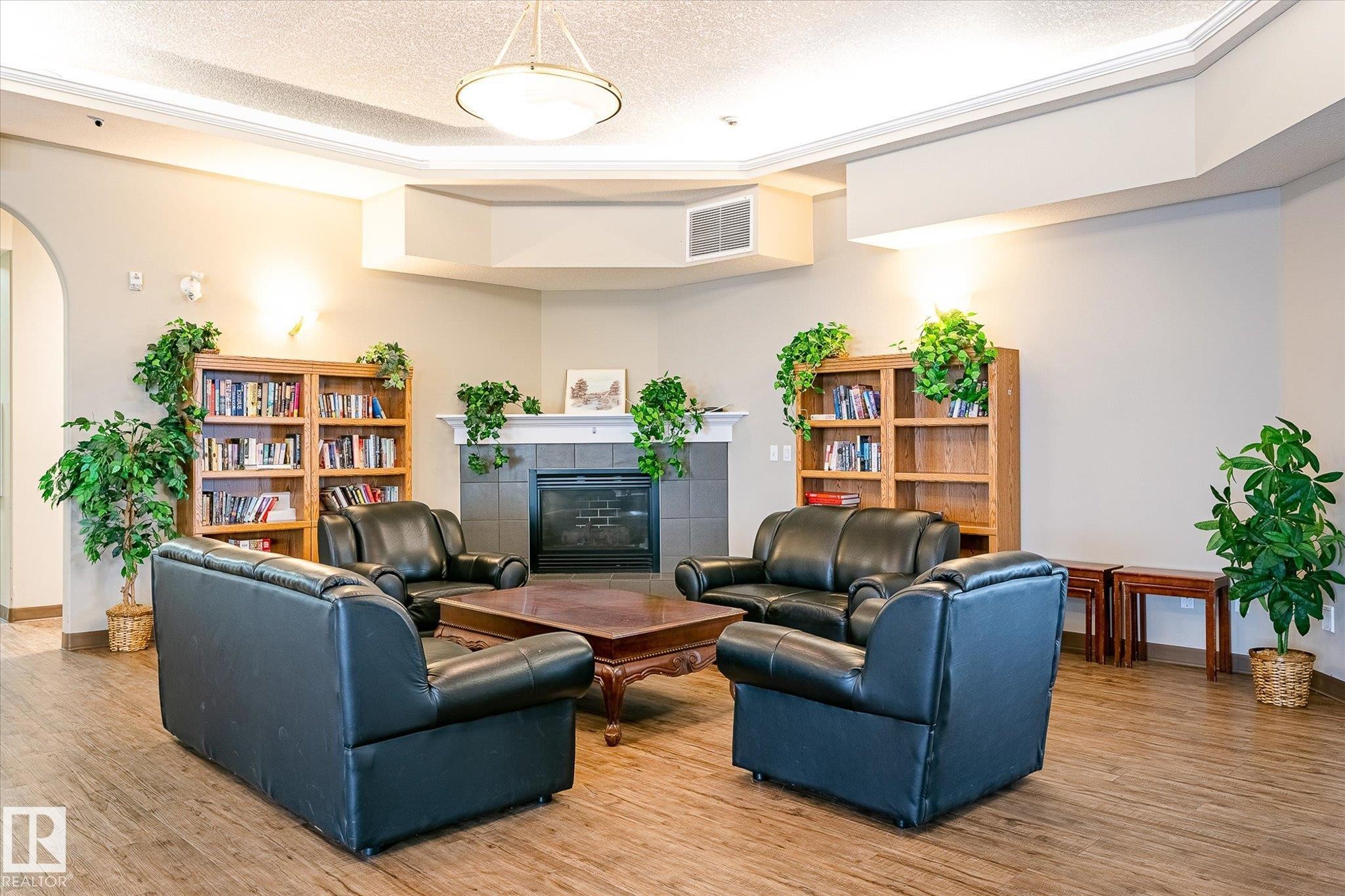 Lounge area featuring a fireplace with tile surround, wood-finish flooring, recessed ceiling with crown molding, and a central chandelier - #310 237 Youville Dr E Nw, Edmonton, AB - Indoor