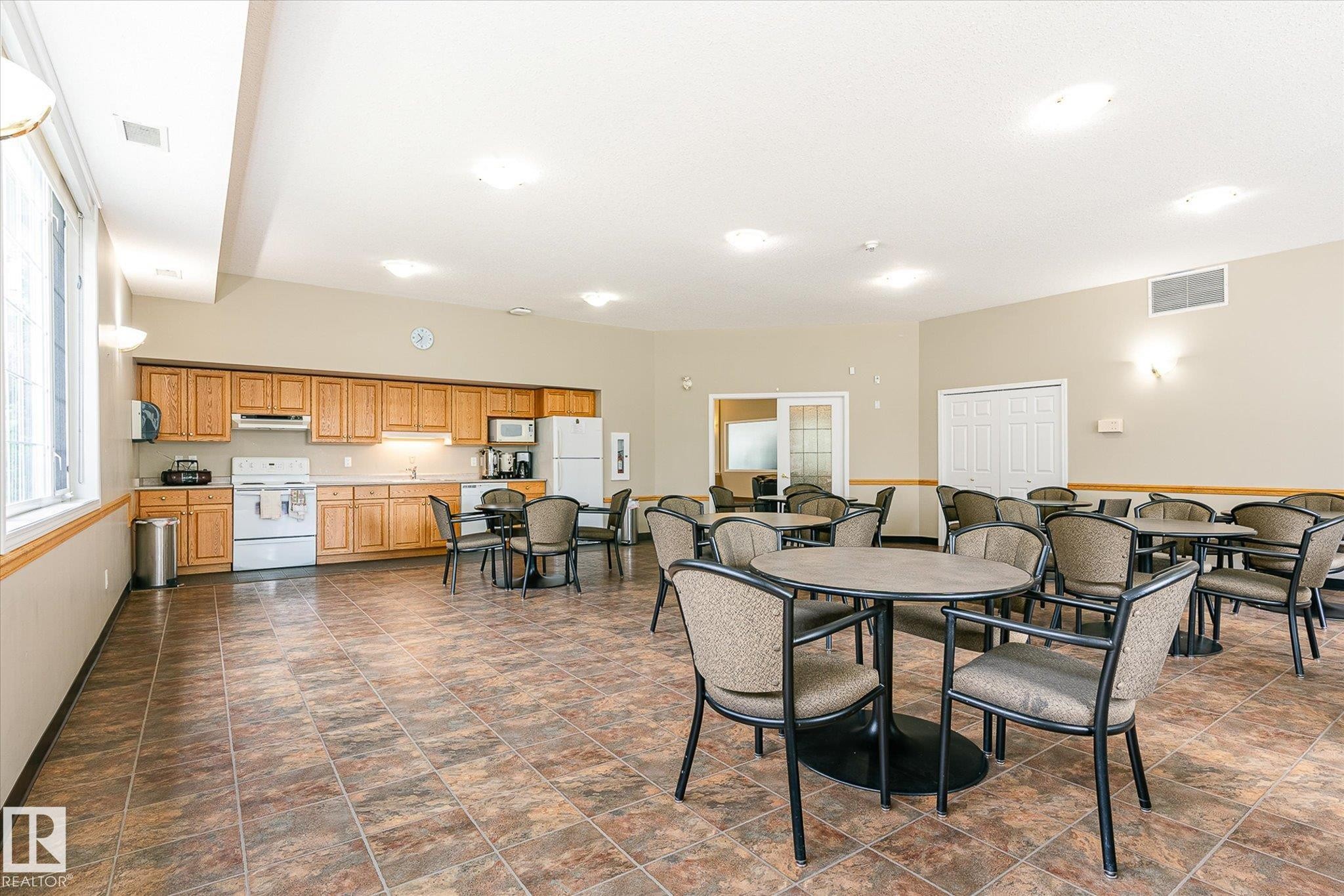 Spacious common area featuring a full kitchen with wood cabinetry, extensive tile flooring, and multiple windows - #310 237 Youville Dr E Nw, Edmonton, AB - Indoor Photo Showing Other Room