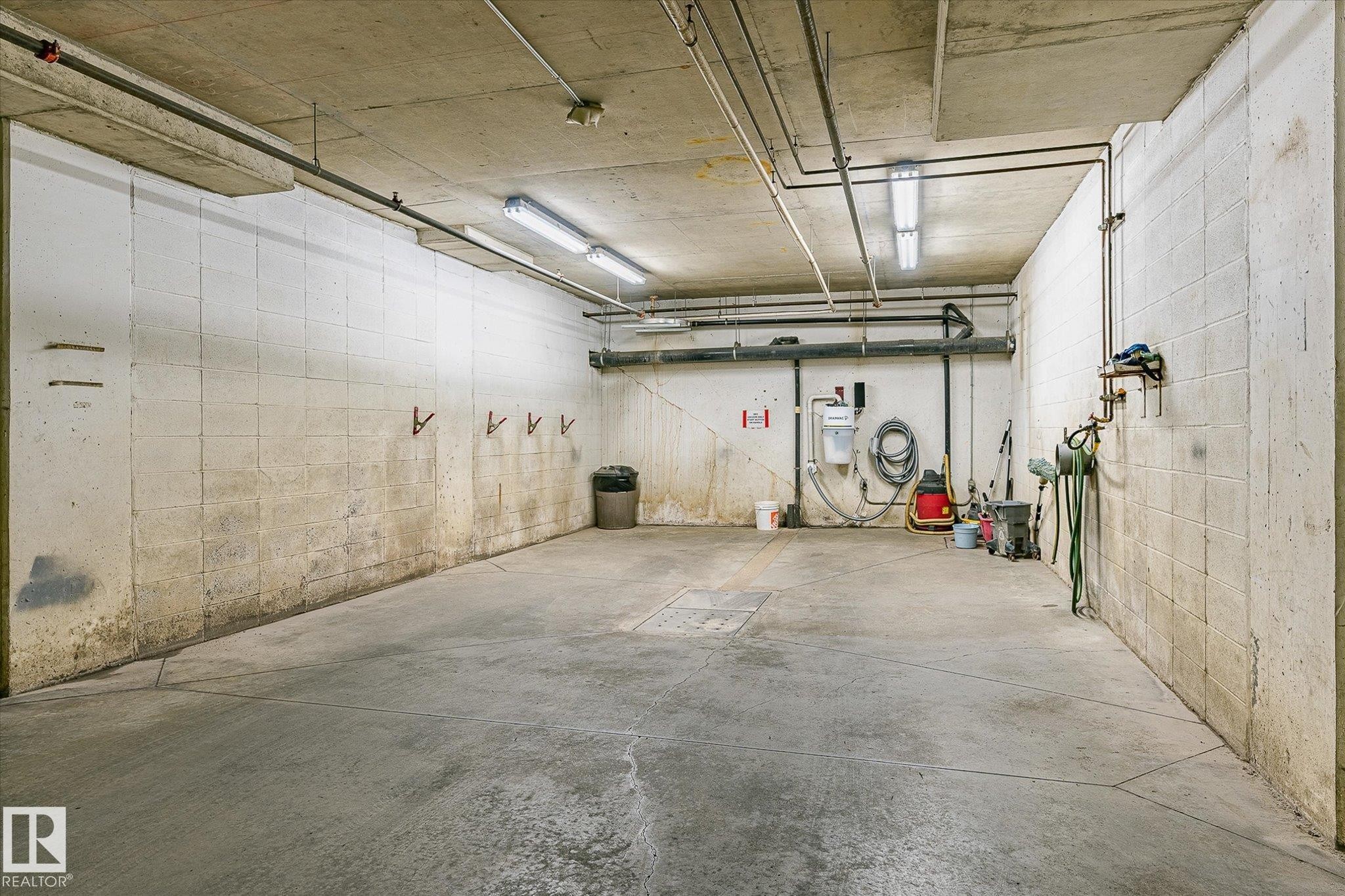 Concrete floor with a visible drainage grate, illuminated by multiple overhead fluorescent light fixtures - #310 237 Youville Dr E Nw, Edmonton, AB - Indoor Photo Showing Garage