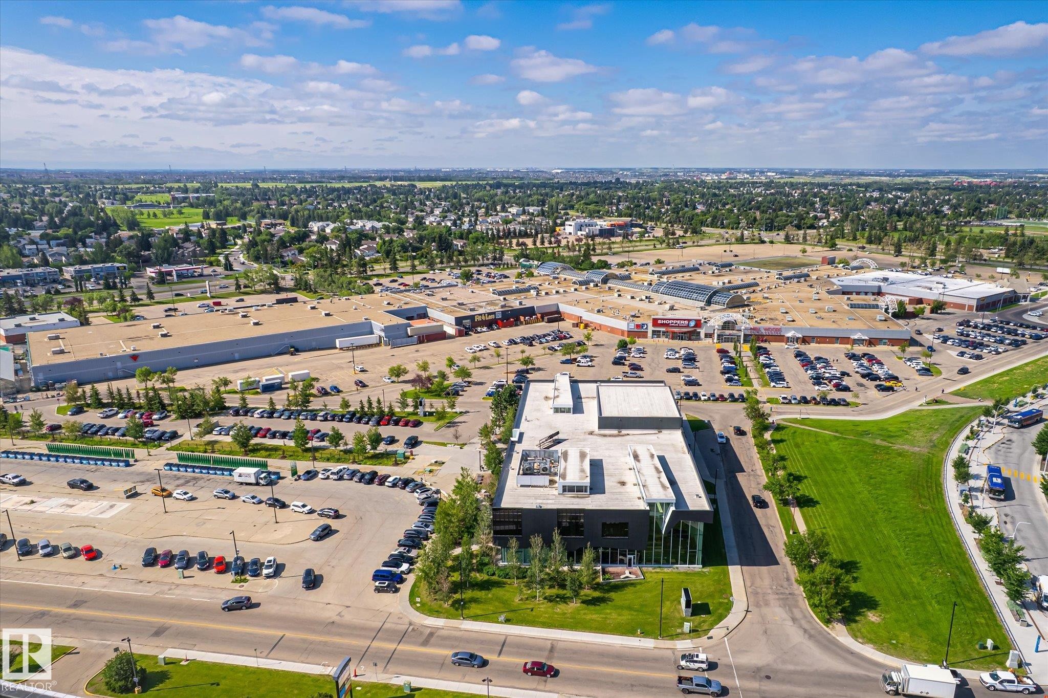 Commercial district featuring multiple retail buildings, expansive paved parking areas, and surrounding green spaces - #310 237 Youville Dr E Nw, Edmonton, AB - Outdoor With View