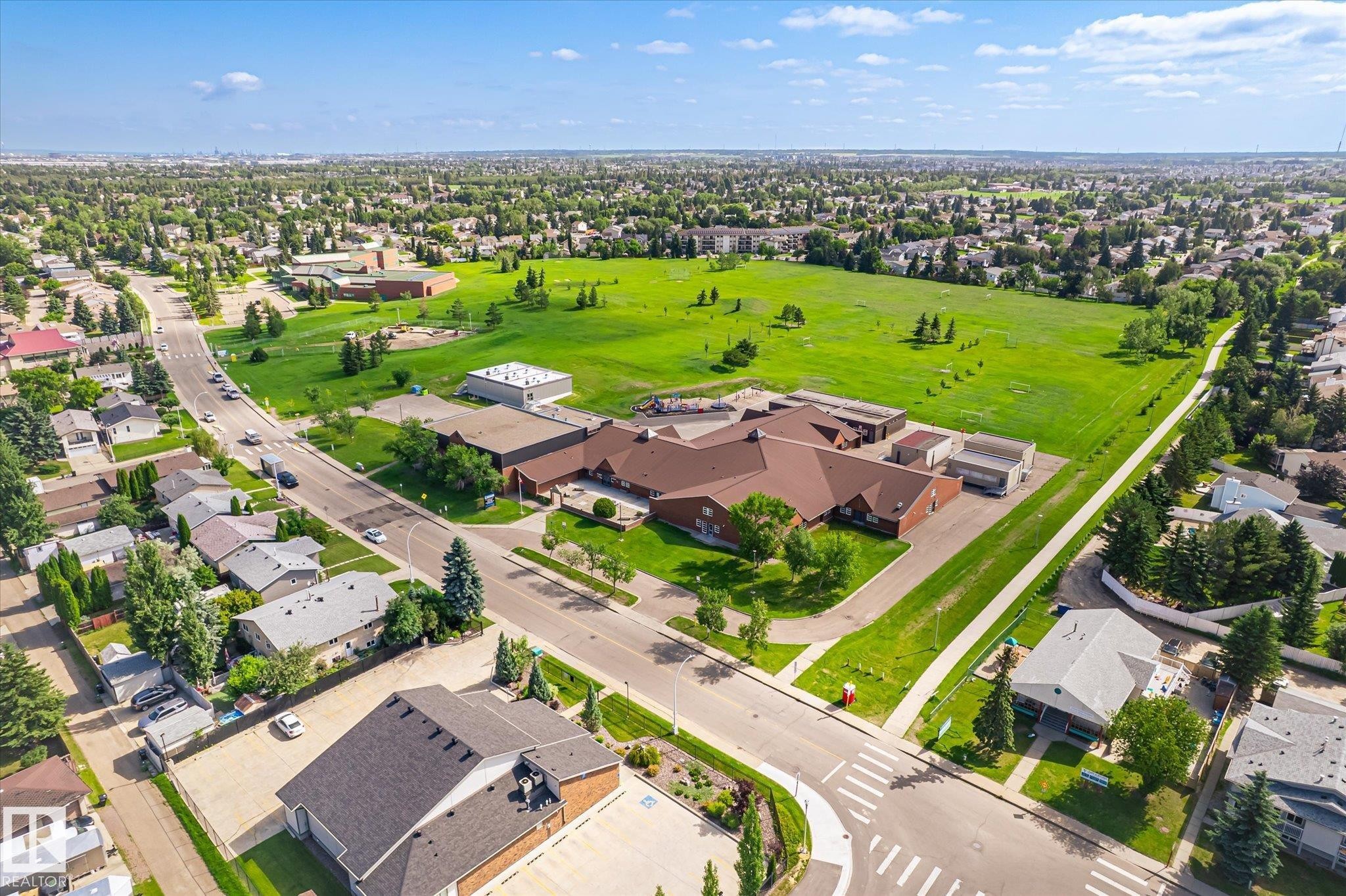 Expansive green space bordering residential properties, featuring mature trees and clear pathways - #310 237 Youville Dr E Nw, Edmonton, AB - Outdoor With View