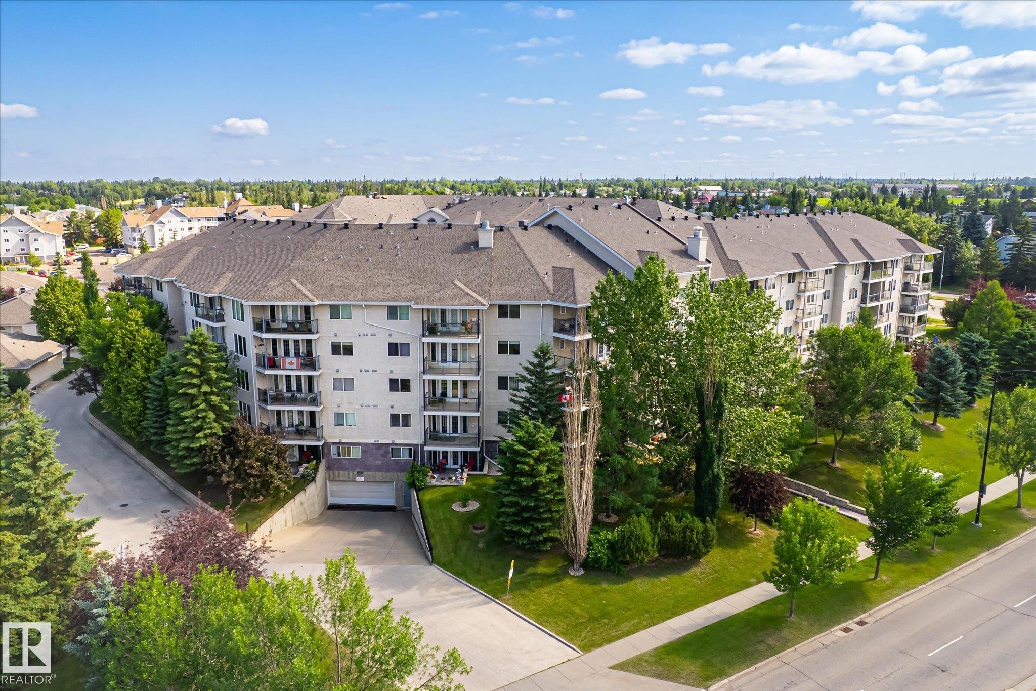 Multi-story residential building featuring balconies, an asphalt shingle roof, and a visible underground parking entrance - #310 237 Youville Dr E Nw, Edmonton, AB - Outdoor