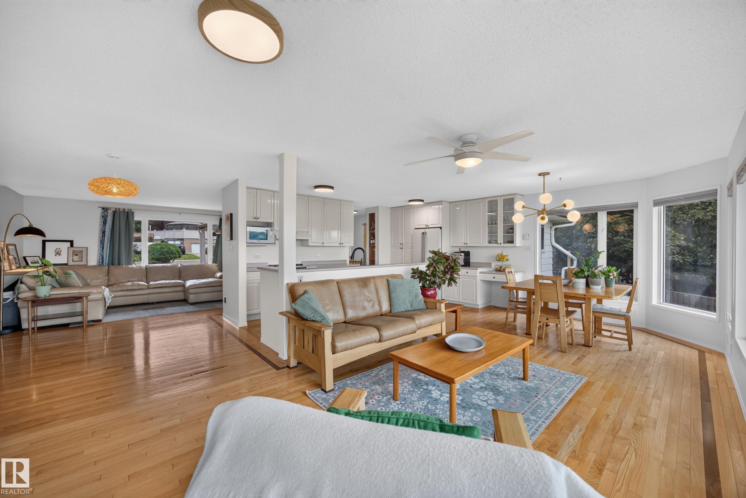 Hardwood flooring throughout a spacious living area, featuring a modern ceiling fan, recessed lighting, and large windows - 3411 103 Avenue Nw, Edmonton, AB