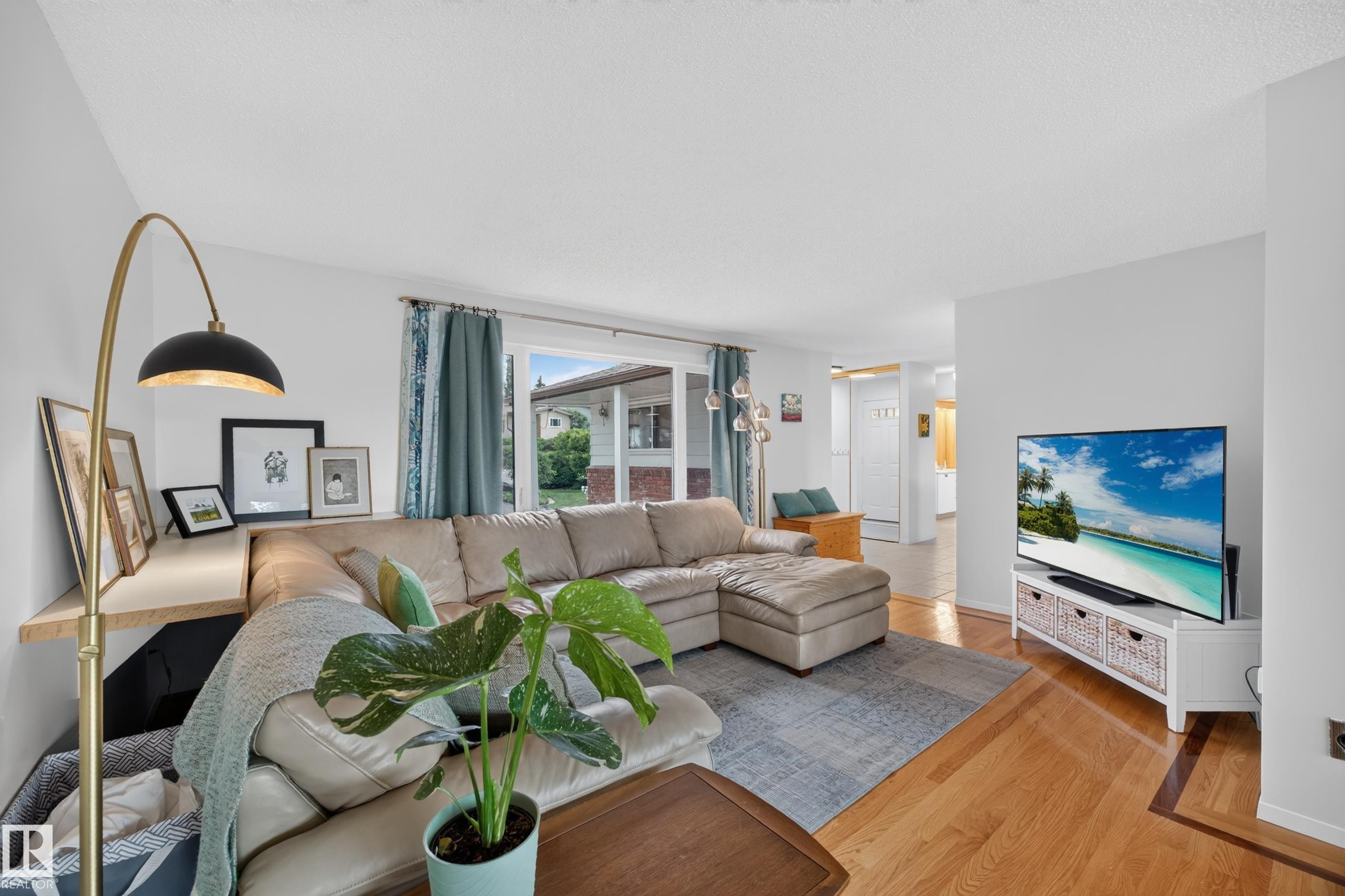 Light-filled living area featuring hardwood flooring, a large window with exterior visibility, a built-in shelf, and recessed lighting - 3411 103 Avenue Nw, Edmonton, AB