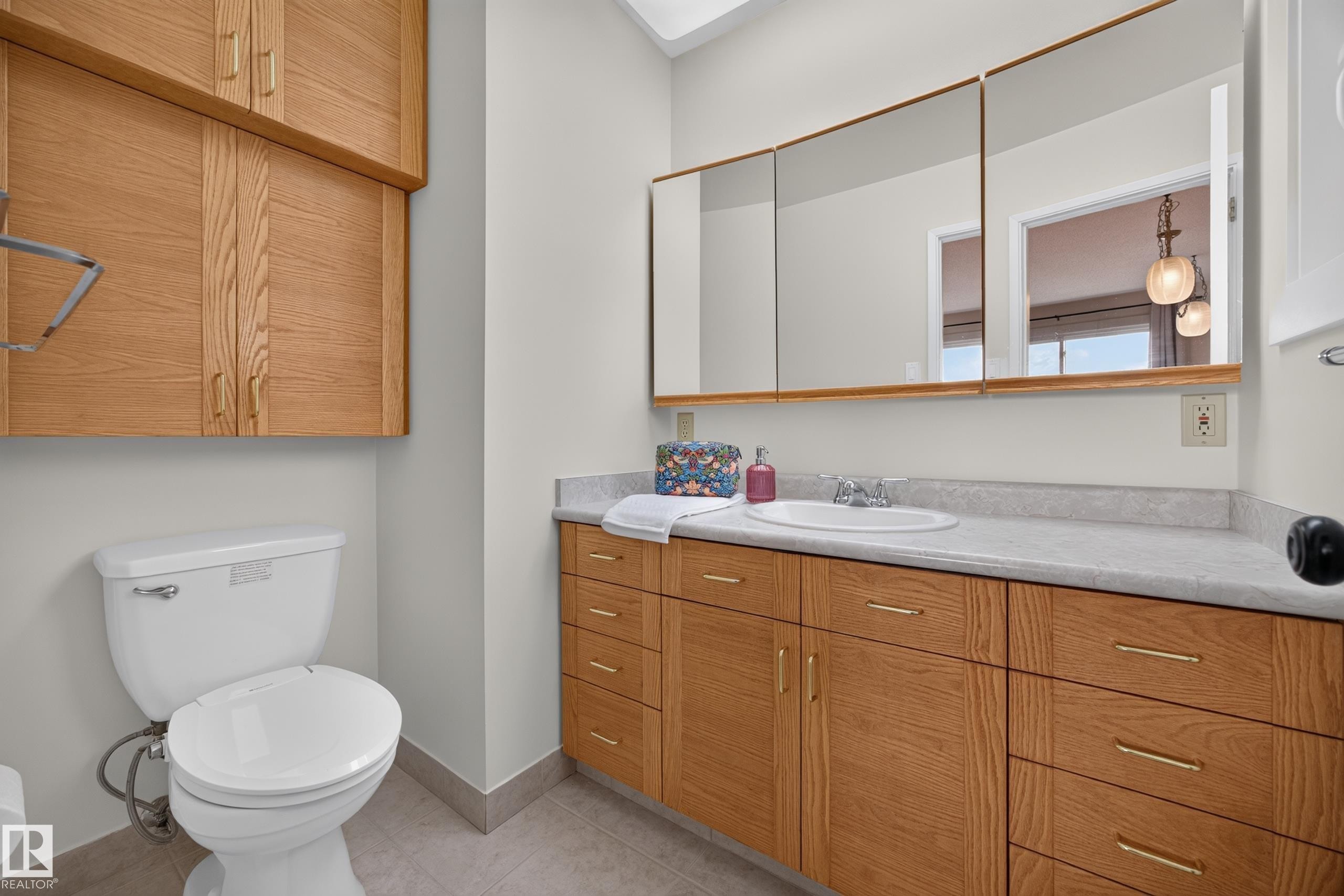Bathroom vanity featuring extensive wood cabinetry with gold-toned hardware, an integrated sink, and a multi-panel mirrored medicine cabinet - 3411 103 Avenue Nw, Edmonton, AB