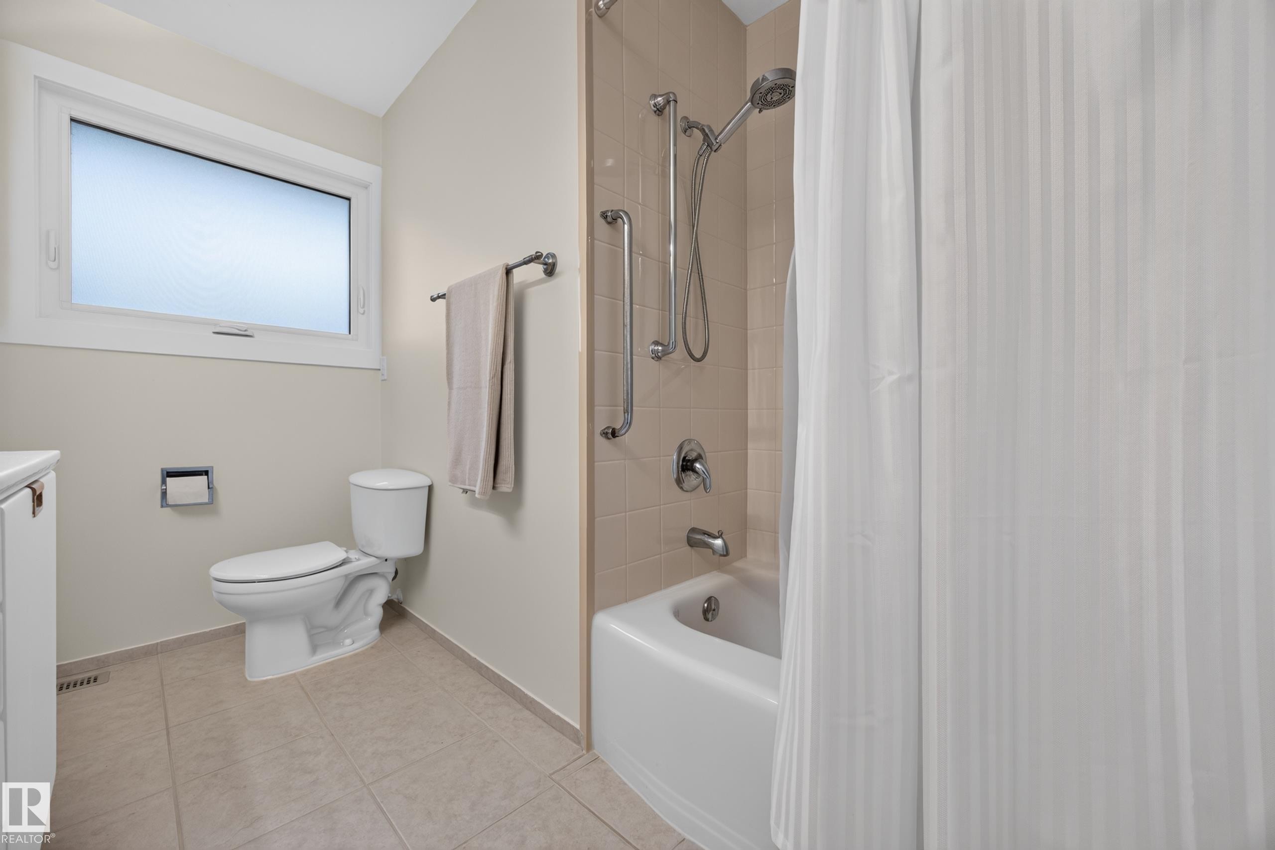Bathroom featuring a white bathtub, ceramic wall tiling, shower grab bar, and a window with privacy glass - 3411 103 Avenue Nw, Edmonton, AB