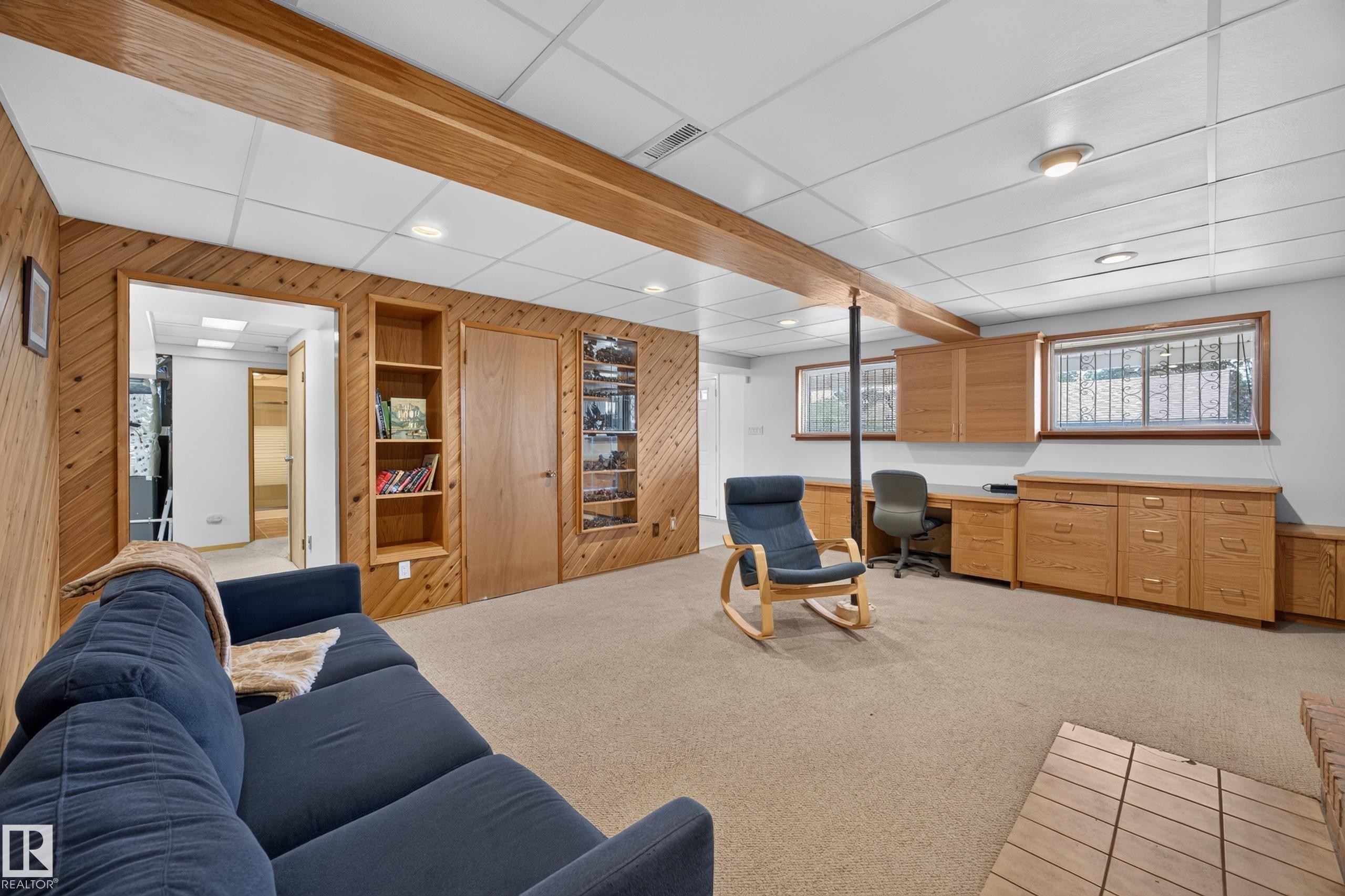 Finished lower level featuring paneled walls, carpet flooring, a drop ceiling with recessed lighting, integrated shelving, and a built-in desk area with cabinetry - 3411 103 Avenue Nw, Edmonton, AB
