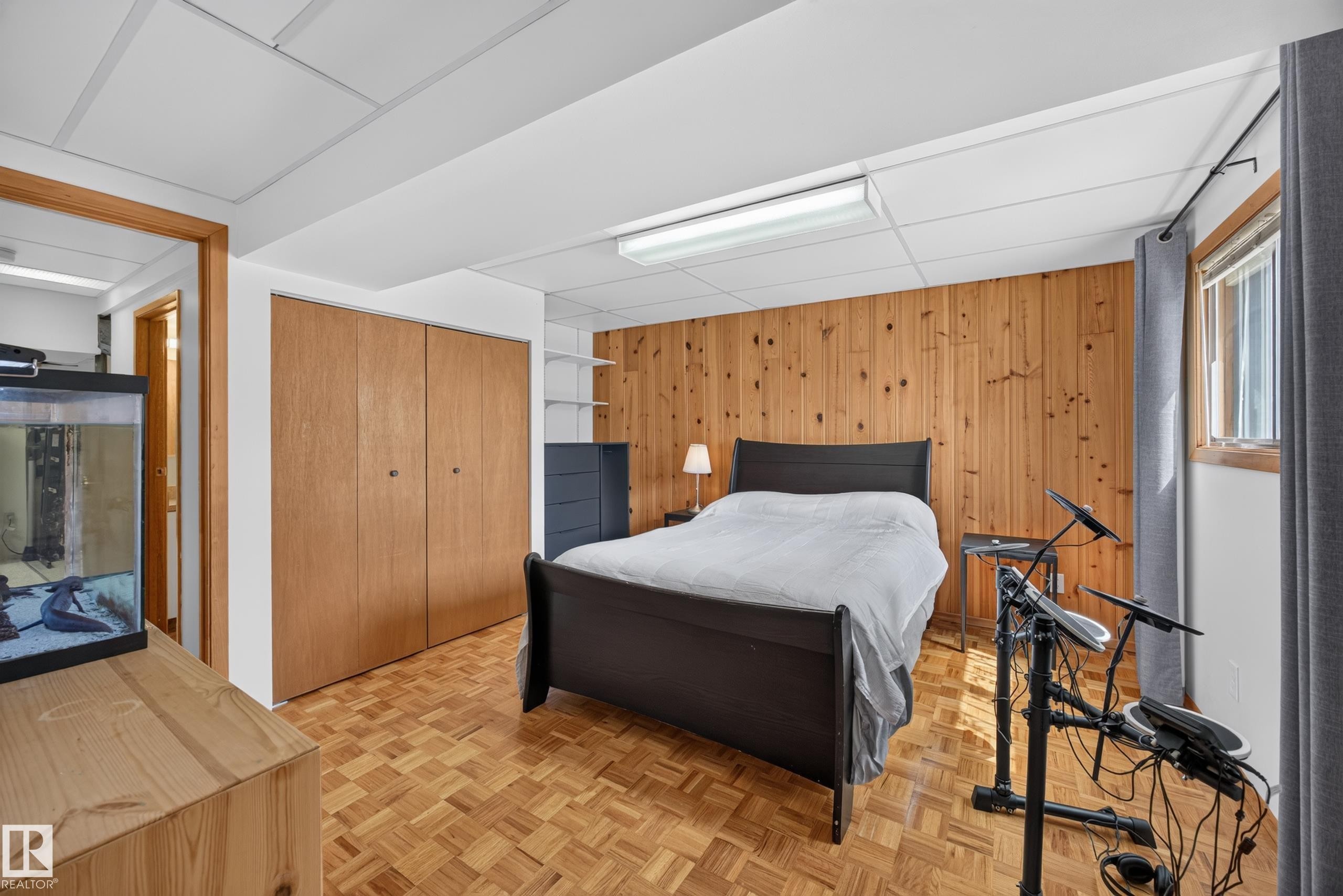 Bedroom featuring wood-finish parquet flooring, wood panel accent wall, recessed lighting, and a large window with privacy blinds - 3411 103 Avenue Nw, Edmonton, AB