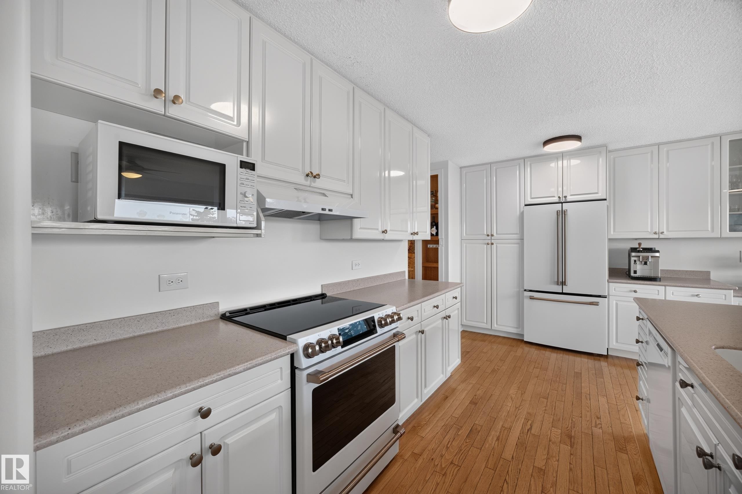 Kitchen featuring extensive white cabinetry, light-toned countertops, wood-finish flooring, a stainless steel range, and a matching refrigerator - 3411 103 Avenue Nw, Edmonton, AB