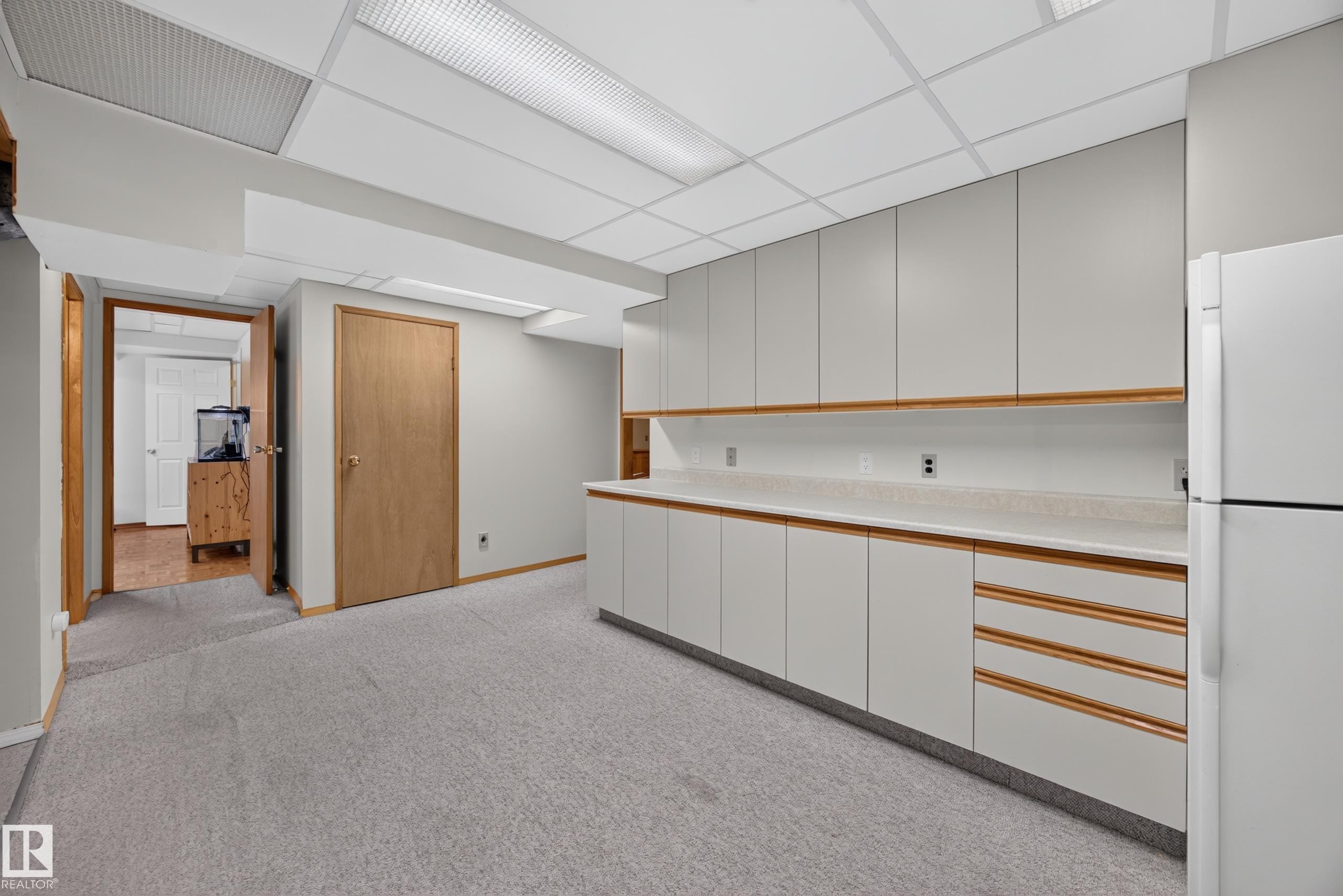 Utility room featuring extensive built-in cabinetry, light-toned countertops, a full-size refrigerator, and textured carpeting - 3411 103 Avenue Nw, Edmonton, AB
