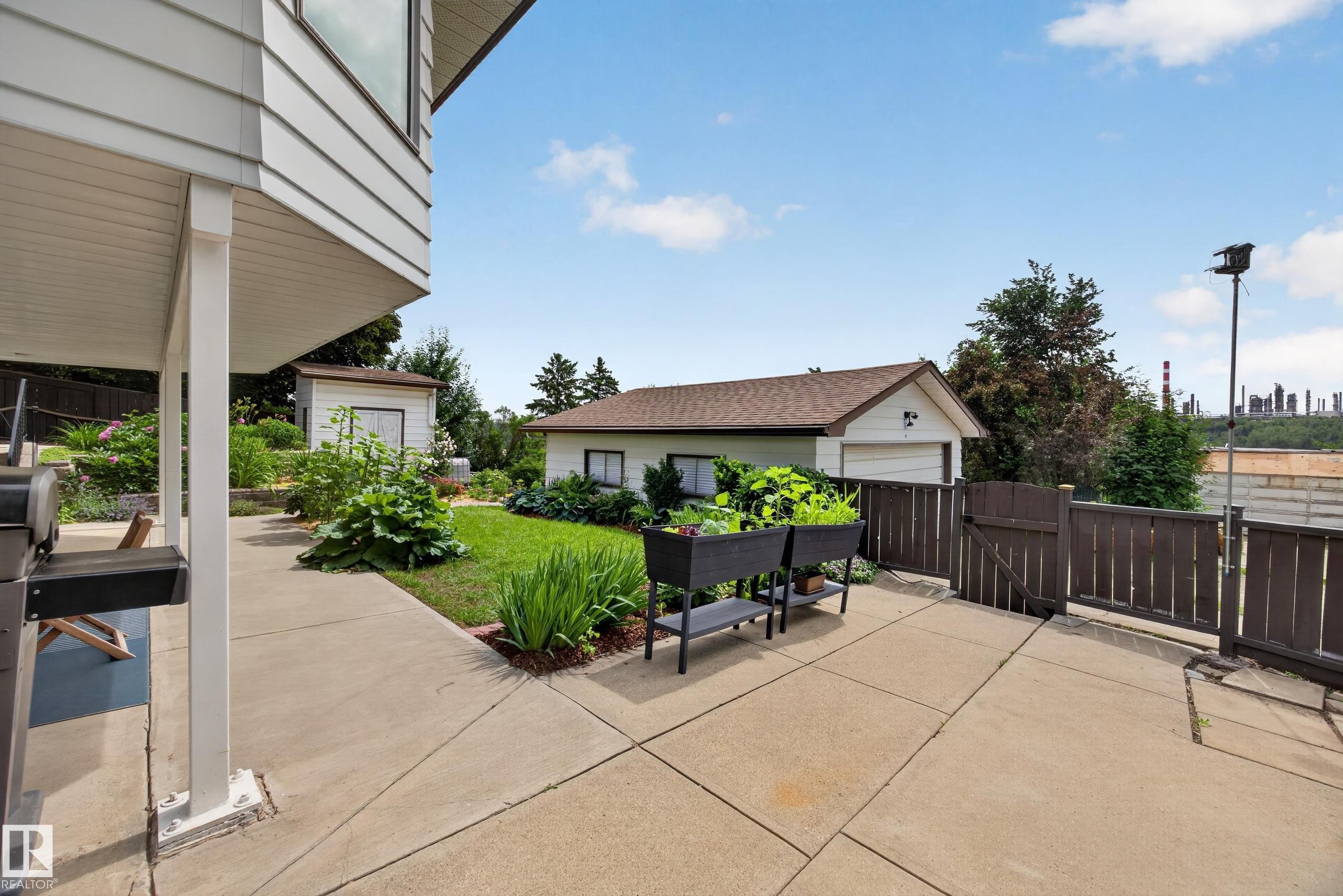 Expansive concrete patio area with a wooden privacy fence and gate, a separate detached garage, and an additional shed - 3411 103 Avenue Nw, Edmonton, AB
