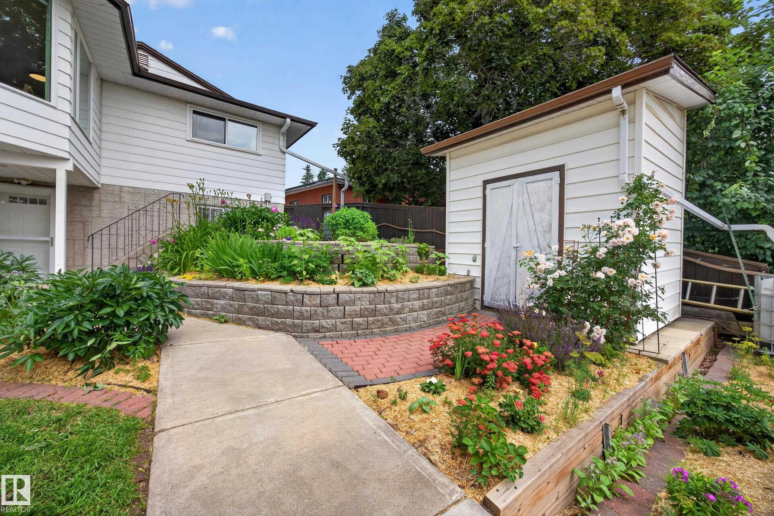 Outdoor landscaping featuring a concrete pathway, a red brick paver section, and two stone-retained garden beds - 3411 103 Avenue Nw, Edmonton, AB