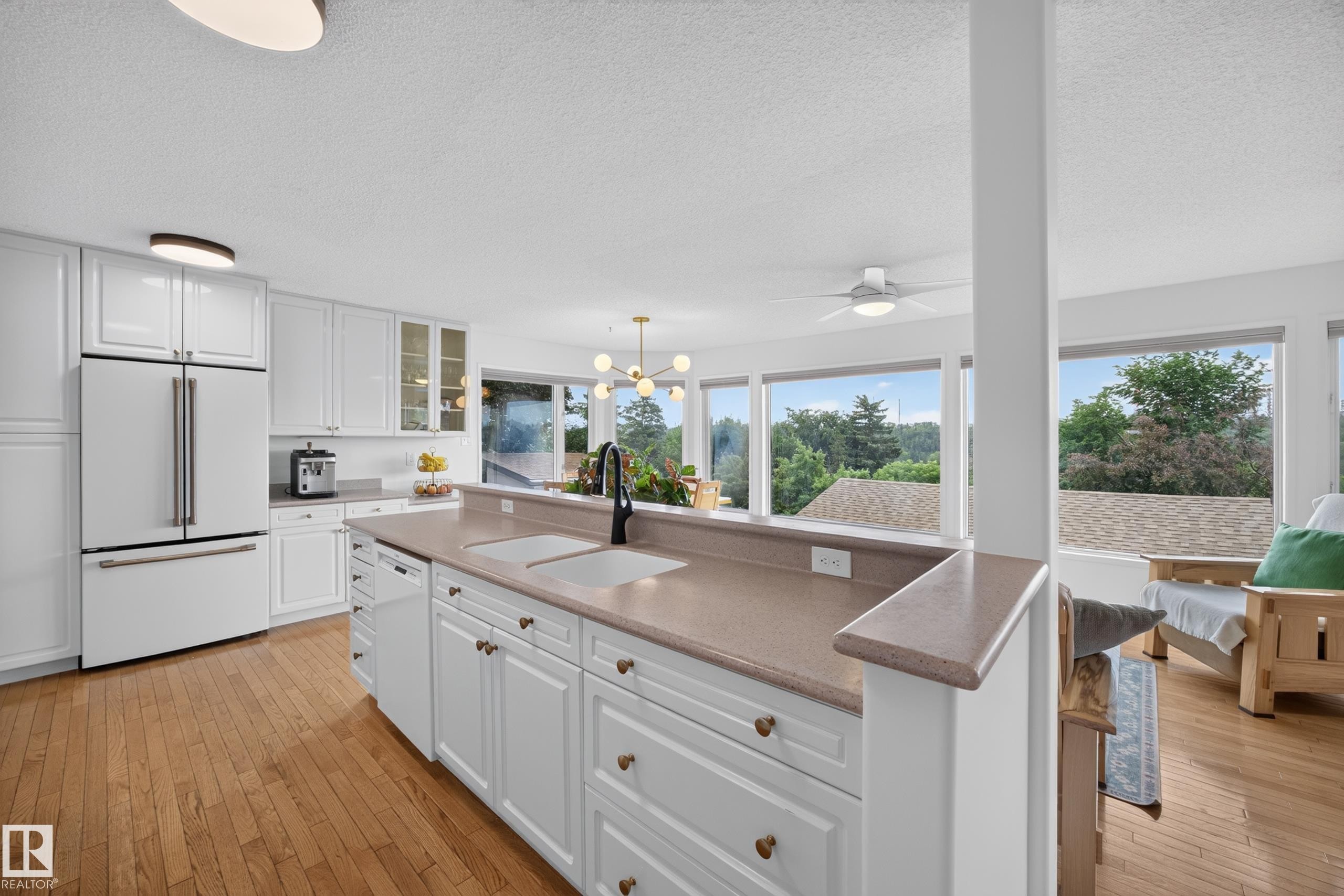 Bright kitchen featuring white cabinetry, wood-finish flooring, a dual basin sink with a black faucet, and a large window wall overlooking exterior scenery - 3411 103 Avenue Nw, Edmonton, AB