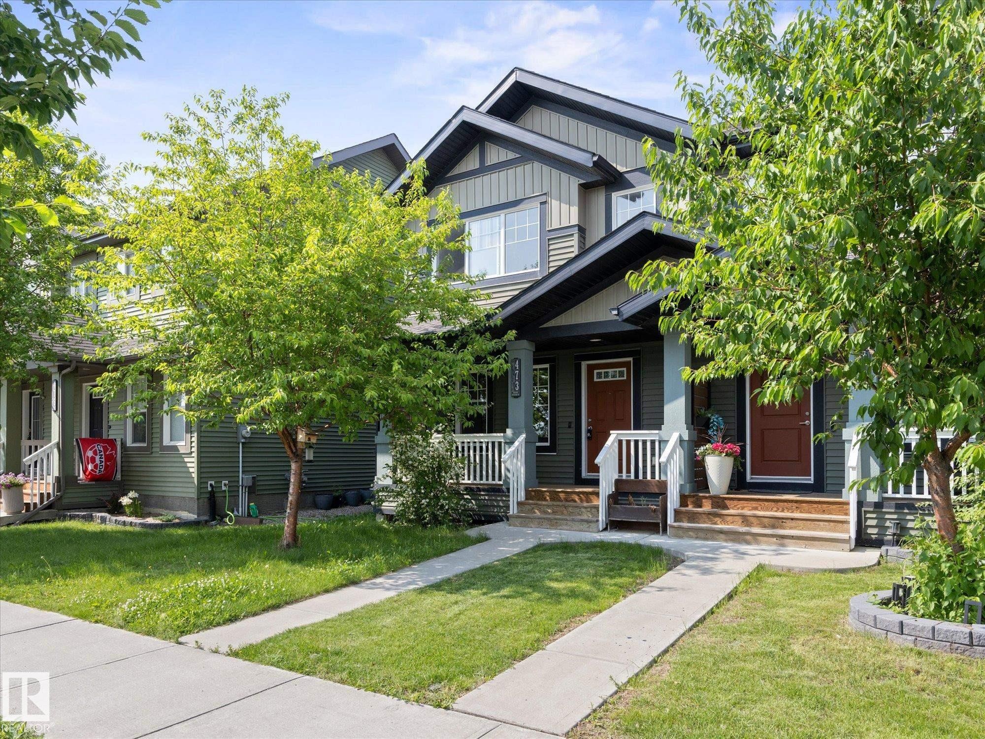 Multi-level townhouse exterior featuring dark green siding, white trim, and a prominent front porch with white railings - 473 Orchards Boulevard Sw, Edmonton, AB - Outdoor With Facade
