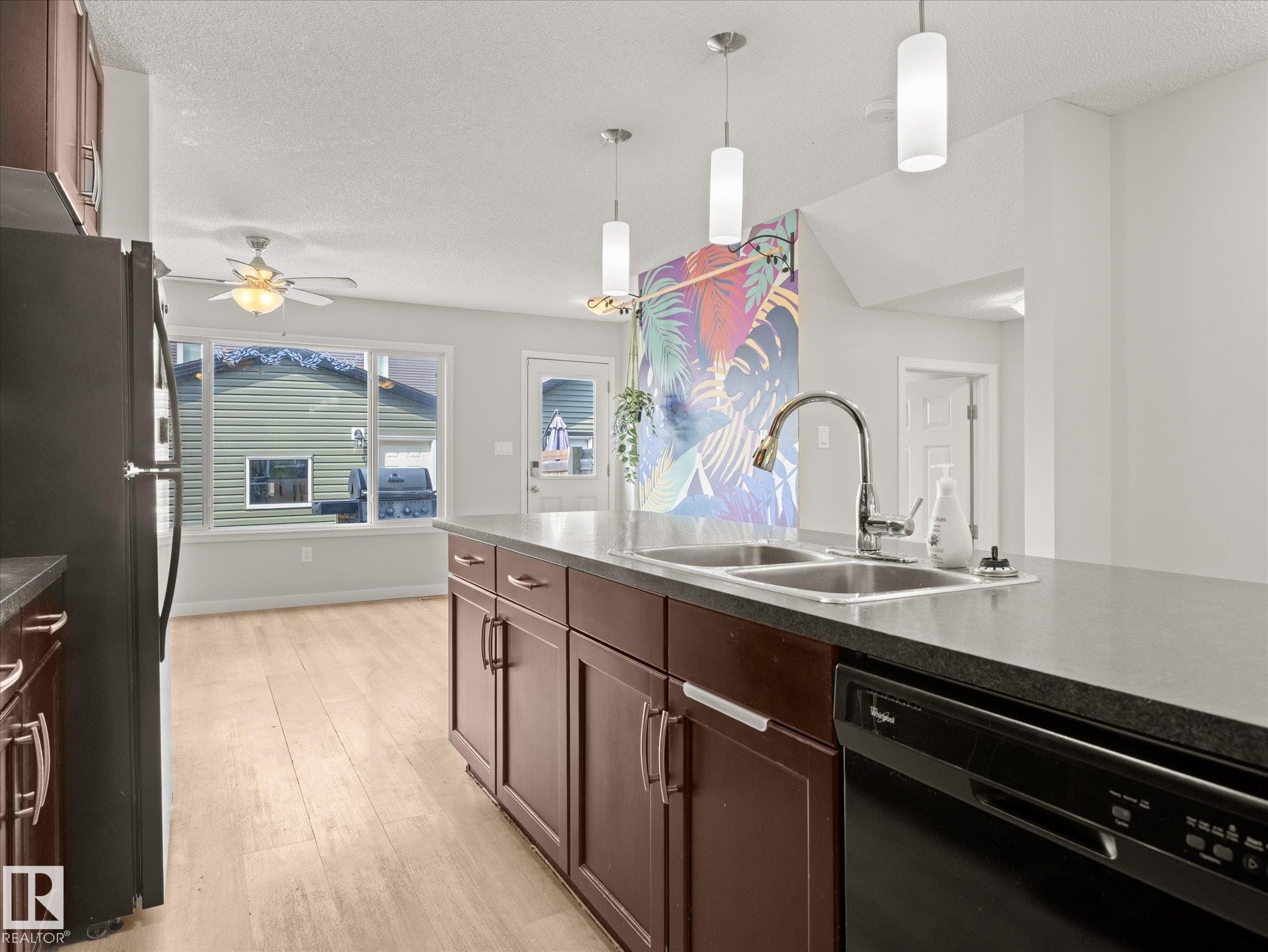 Kitchen island featuring a double basin sink with a high-arc faucet, integrated dishwasher, and dark cabinetry with modern hardware - 473 Orchards Boulevard Sw, Edmonton, AB - Indoor Photo Showing Kitchen With Double Sink