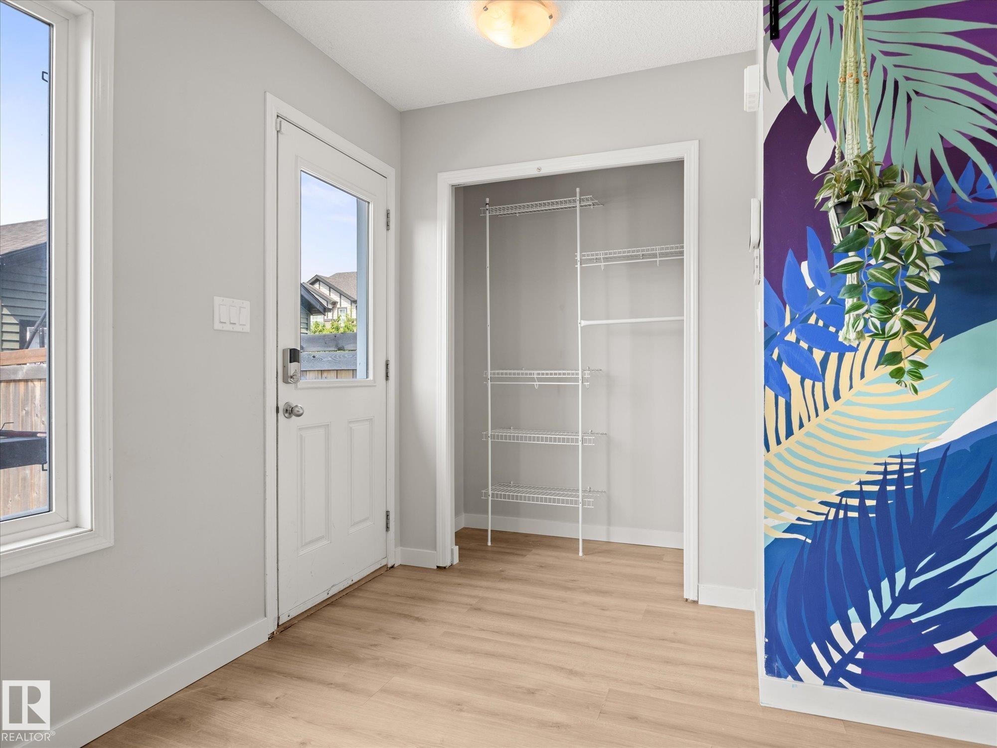 Entryway featuring a glass-paneled door, wood-finish flooring, white trim, a built-in closet with wire shelving, and a decorative wall accent - 473 Orchards Boulevard Sw, Edmonton, AB - Indoor Photo Showing Other Room