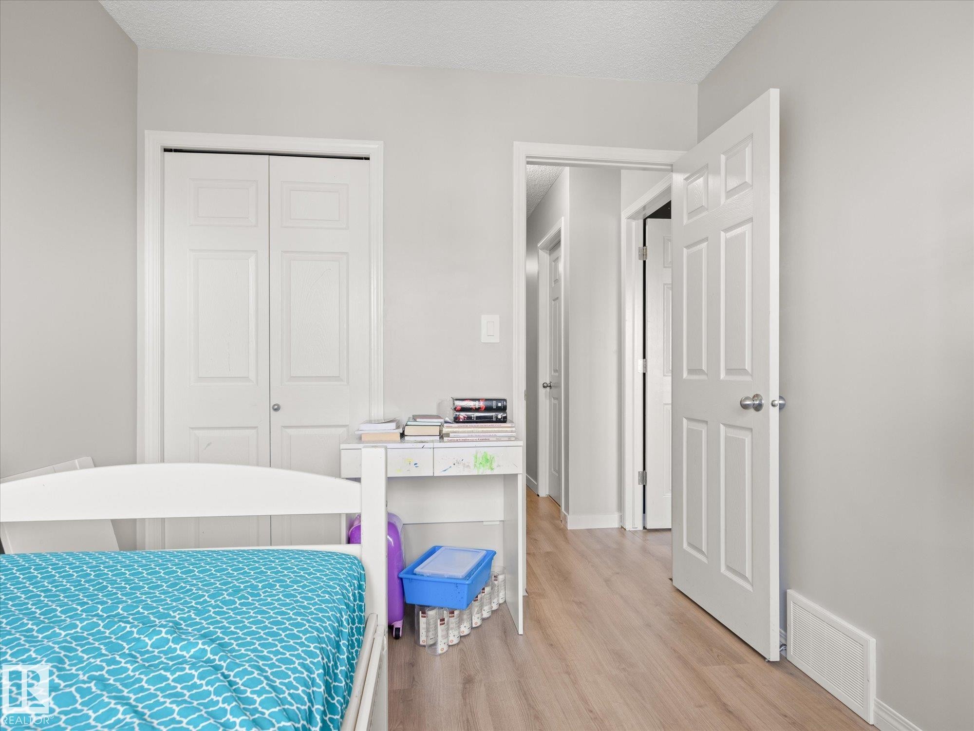 Neutral-toned interior featuring wood-finish flooring, white trim, and a white six-panel interior door - 473 Orchards Boulevard Sw, Edmonton, AB - Indoor Photo Showing Bedroom