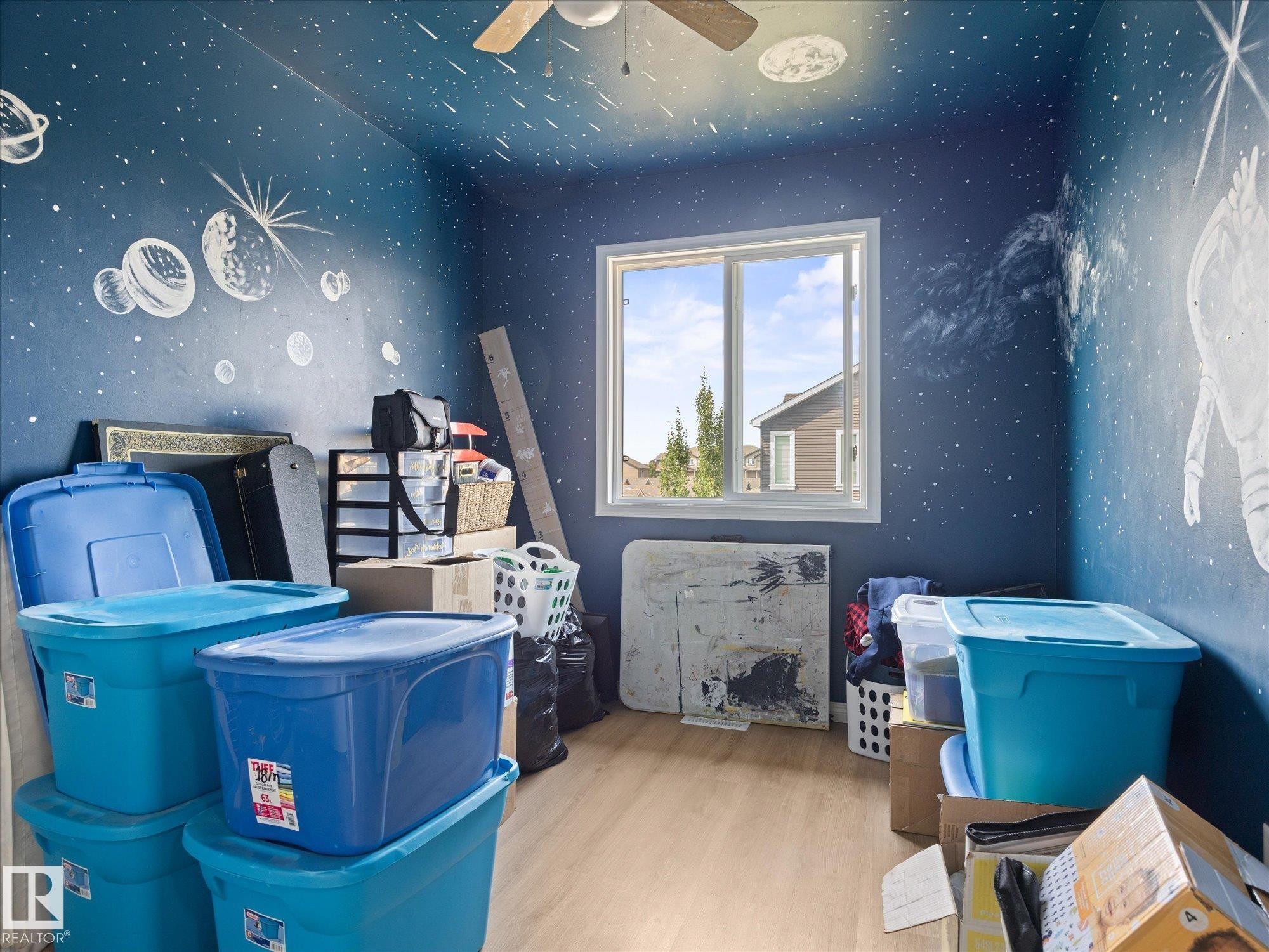 Room featuring a double-pane window, blue walls with painted celestial elements, light wood-finish flooring, and a ceiling fan - 473 Orchards Boulevard Sw, Edmonton, AB - Indoor Photo Showing Other Room