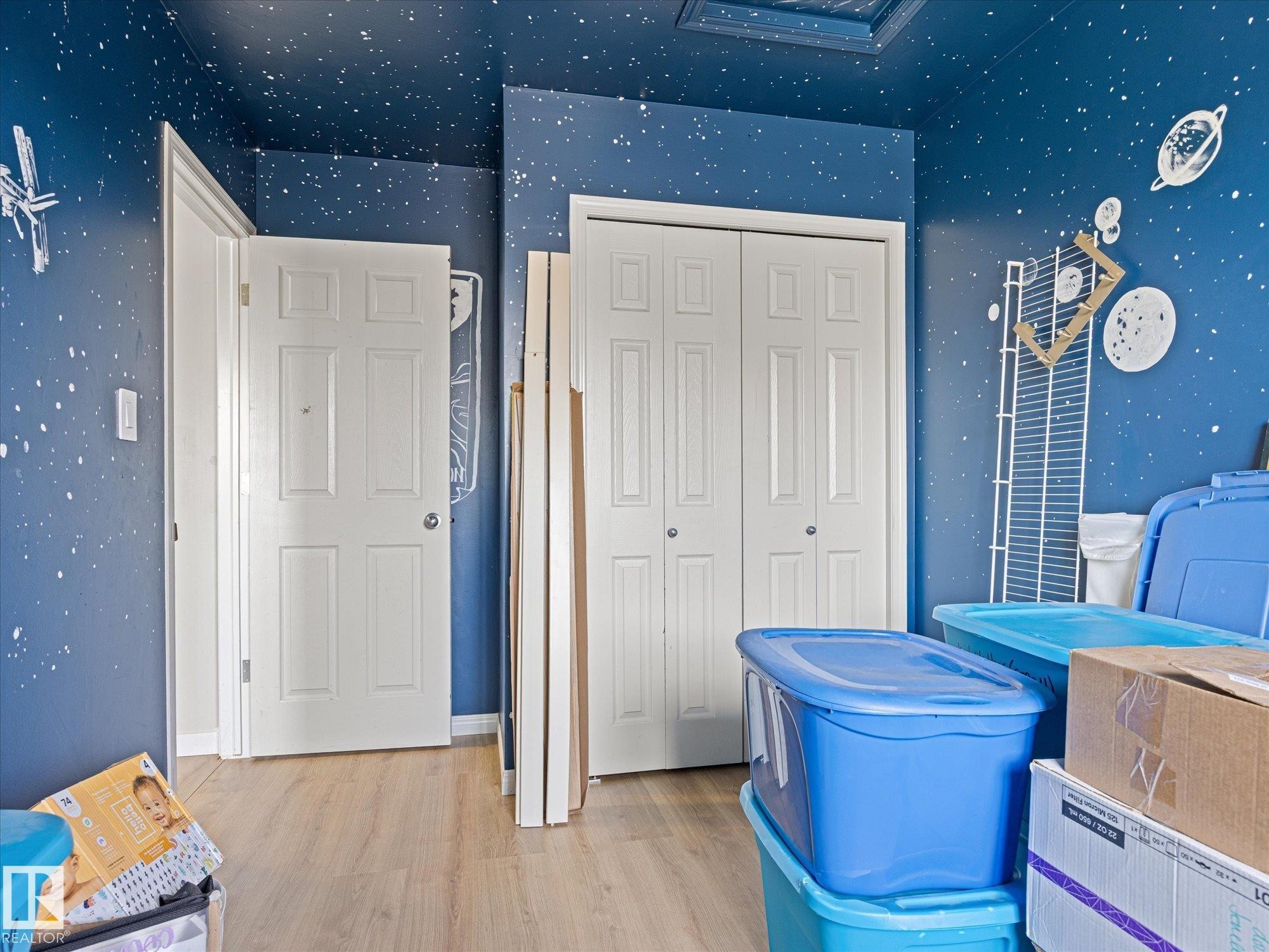 Room featuring light wood-finish flooring, a white paneled door, and a white bi-fold closet door - 473 Orchards Boulevard Sw, Edmonton, AB - Indoor