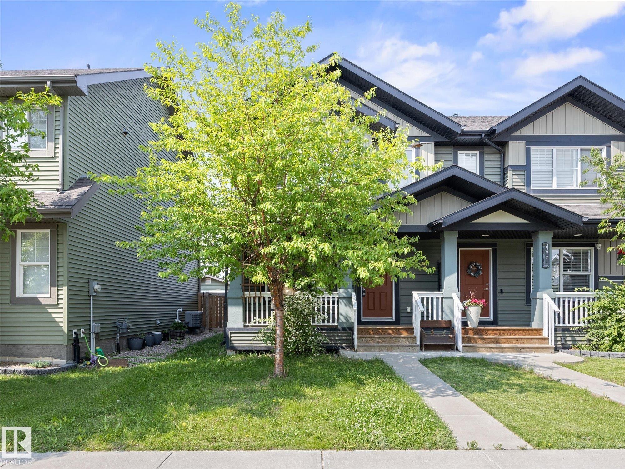 Contemporary townhome exterior featuring multi-toned siding, gabled rooflines, white railing accents, and a sidewalk entrance - 473 Orchards Boulevard Sw, Edmonton, AB - Outdoor With Facade