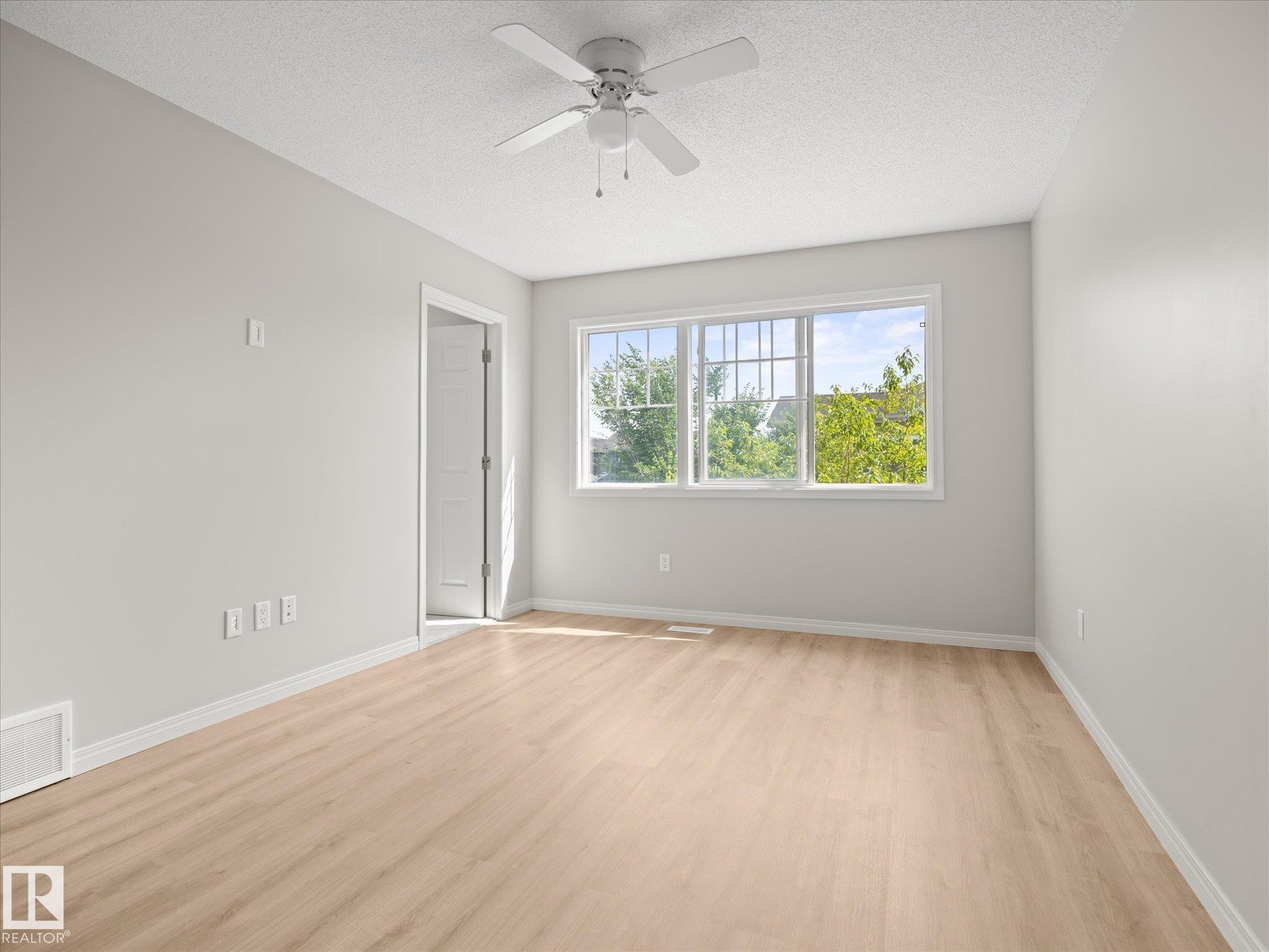 Bright room featuring light-toned wood-finish flooring, a contemporary ceiling fan, and a large multi-pane window - 473 Orchards Boulevard Sw, Edmonton, AB - Indoor Photo Showing Other Room