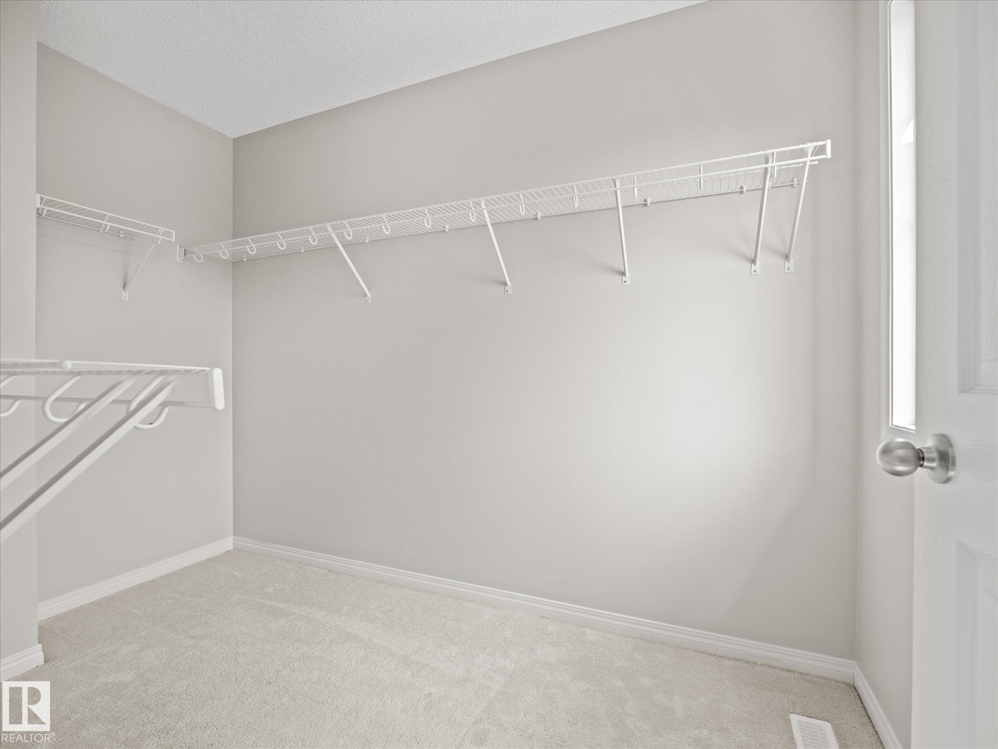 Walk-in closet featuring light gray walls, white wire shelving, light-colored carpeting, and a white paneled door with a brushed nickel knob - 473 Orchards Boulevard Sw, Edmonton, AB - Indoor With Storage
