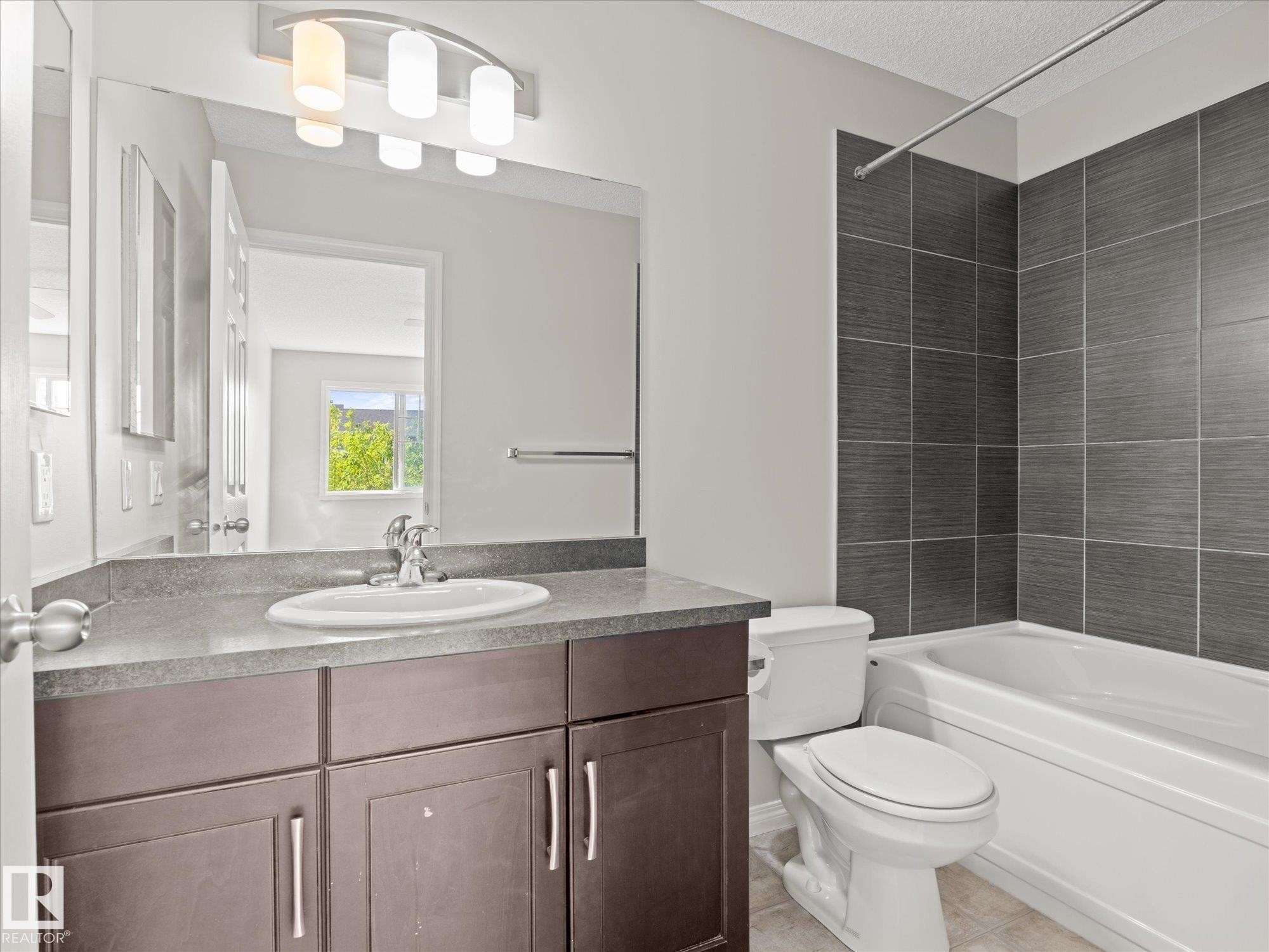 Bathroom featuring a dark wood-finish vanity with a light countertop, an under-mounted sink with a chrome faucet, and a large wall mirror - 473 Orchards Boulevard Sw, Edmonton, AB - Indoor Photo Showing Bathroom