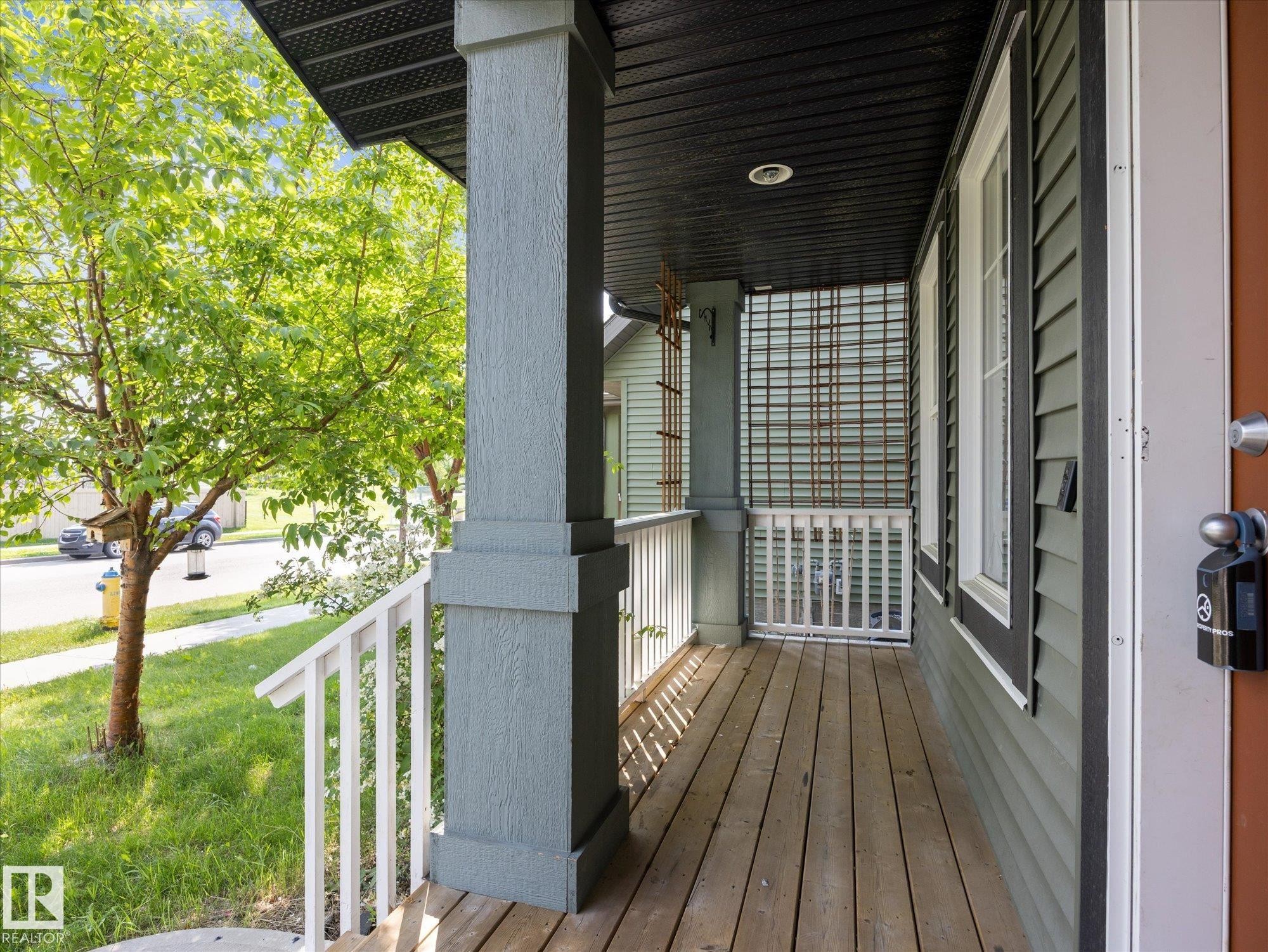 Inviting front porch featuring wood-finish flooring, white railings, and a prominent support column - 473 Orchards Boulevard Sw, Edmonton, AB - Outdoor With Exterior