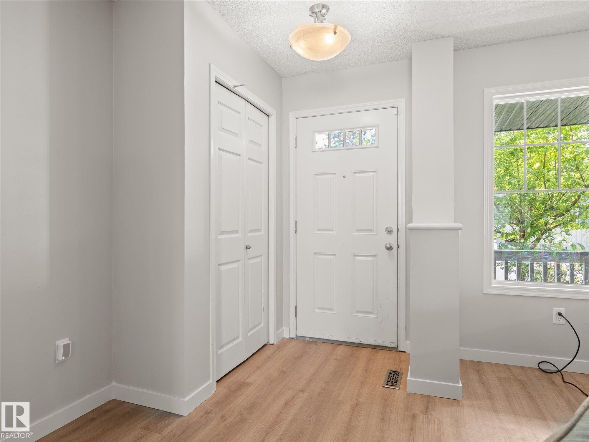 Entryway featuring wood-finish flooring, a white paneled front door with decorative glass inserts, and a double-door closet with louvered panels - 473 Orchards Boulevard Sw, Edmonton, AB - Indoor Photo Showing Other Room