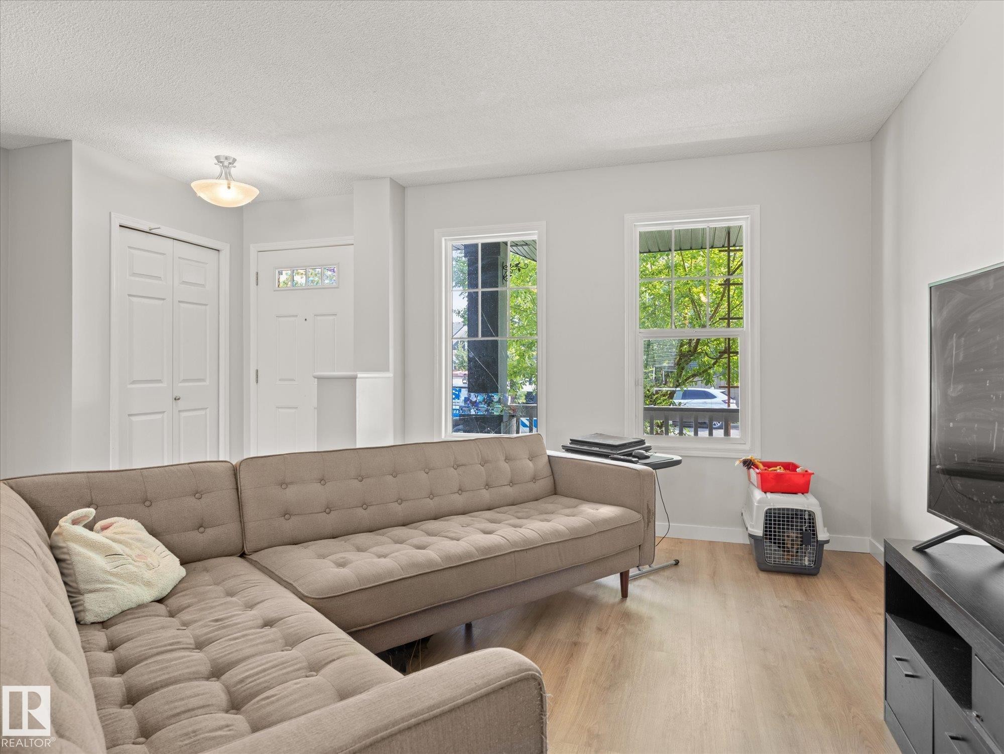Living area featuring wood-finish flooring, white walls, and a front entry door with decorative glass - 473 Orchards Boulevard Sw, Edmonton, AB - Indoor Photo Showing Living Room