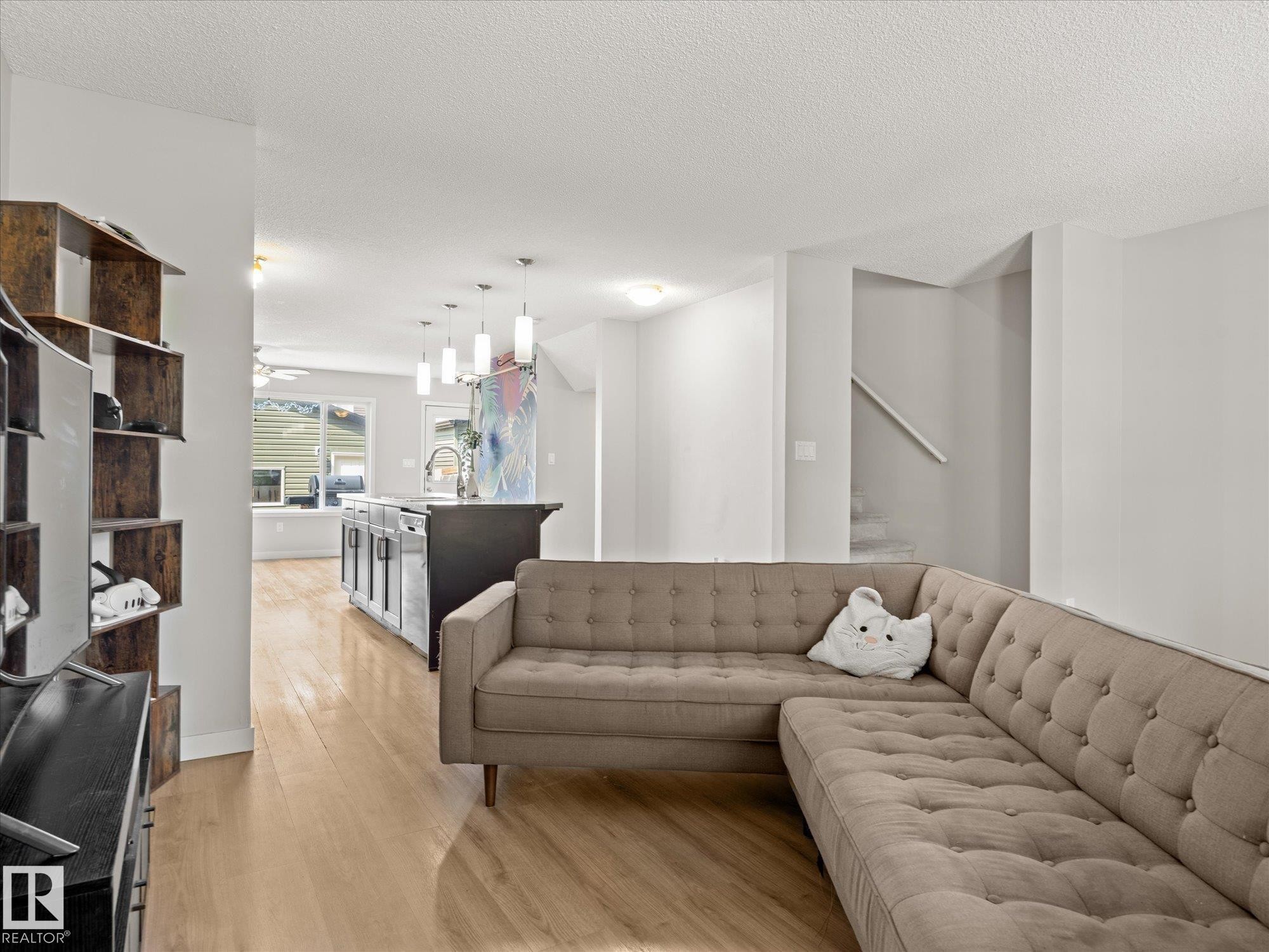 Open-concept living space featuring wood-finish flooring, a kitchen island with pendant lighting, and a staircase - 473 Orchards Boulevard Sw, Edmonton, AB - Indoor Photo Showing Living Room