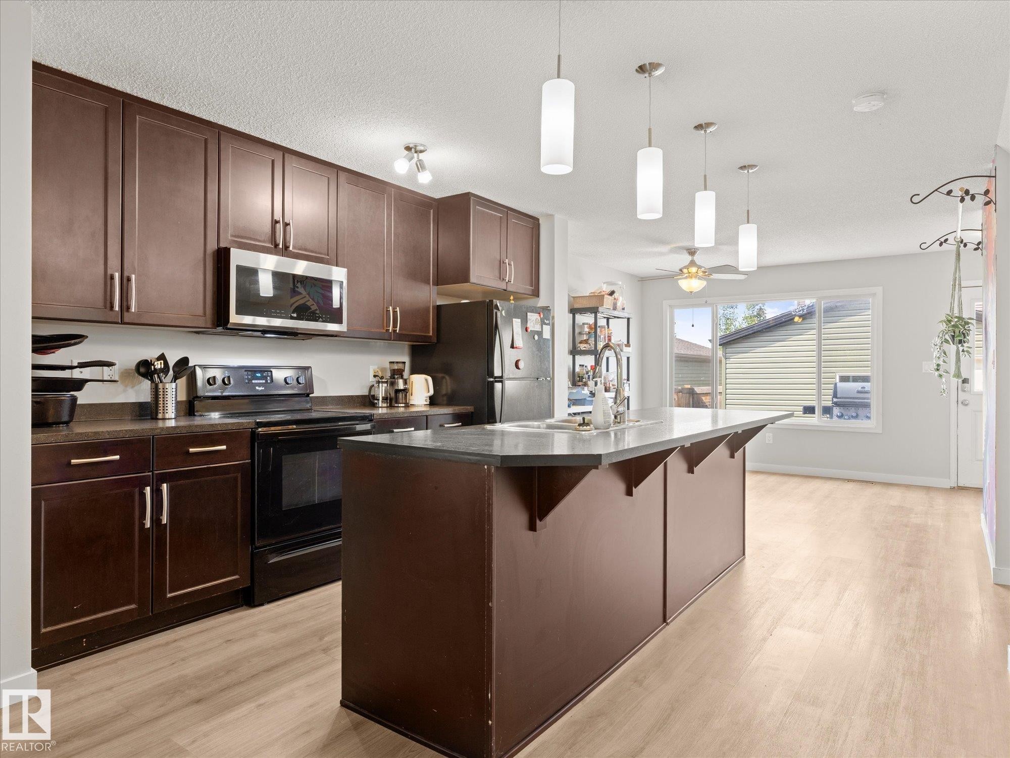 Kitchen featuring rich wood-finish cabinetry, a central island with seating, dark countertops, stainless steel appliances, and wood-finish flooring - 473 Orchards Boulevard Sw, Edmonton, AB - Indoor Photo Showing Kitchen With Upgraded Kitchen