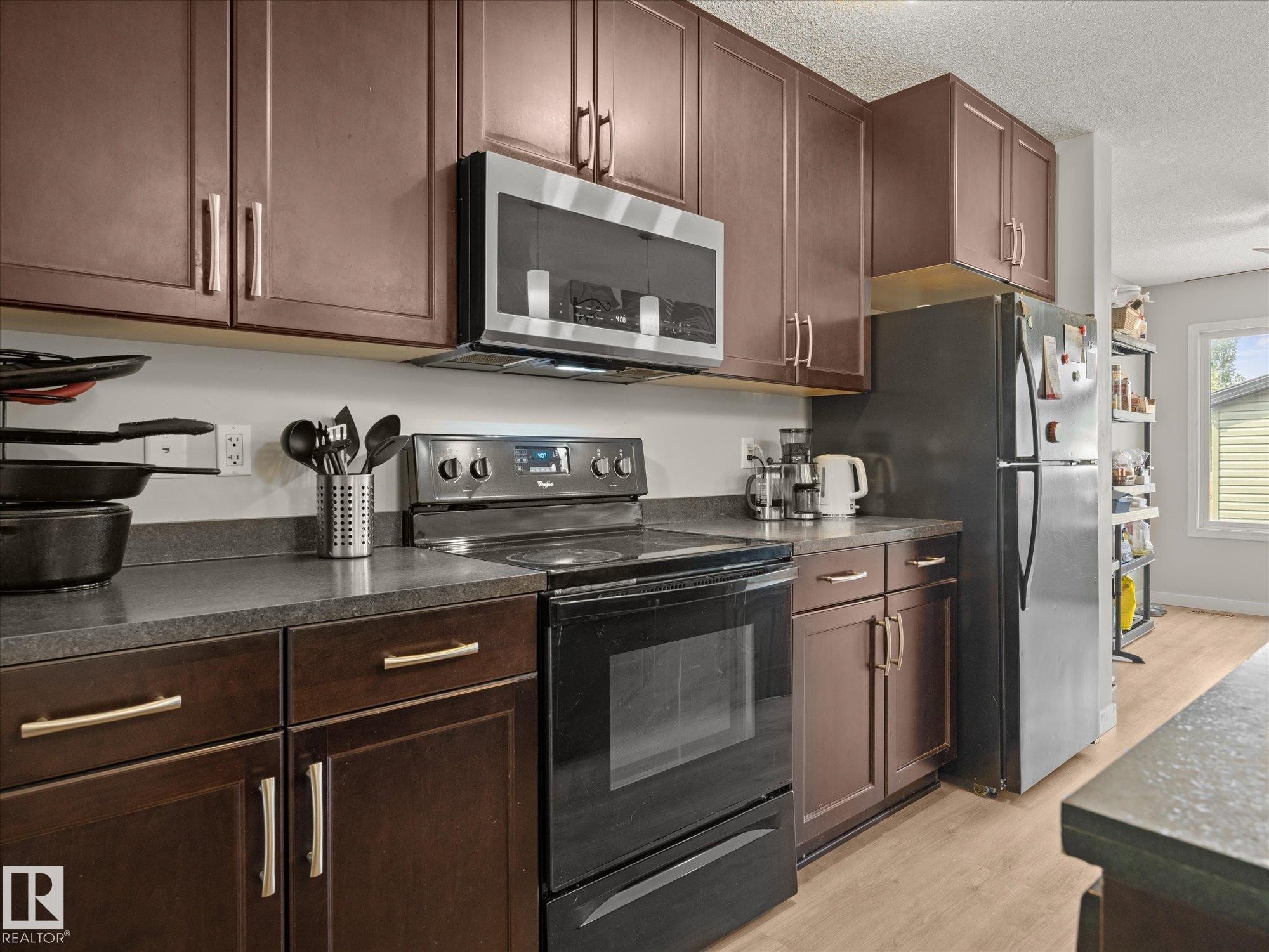 Kitchen featuring dark wood-finish cabinetry with brushed metal hardware, dark countertops, and stainless steel appliances including a refrigerator, microwave, and electric range - 473 Orchards Boulevard Sw, Edmonton, AB - Indoor Photo Showing Kitchen