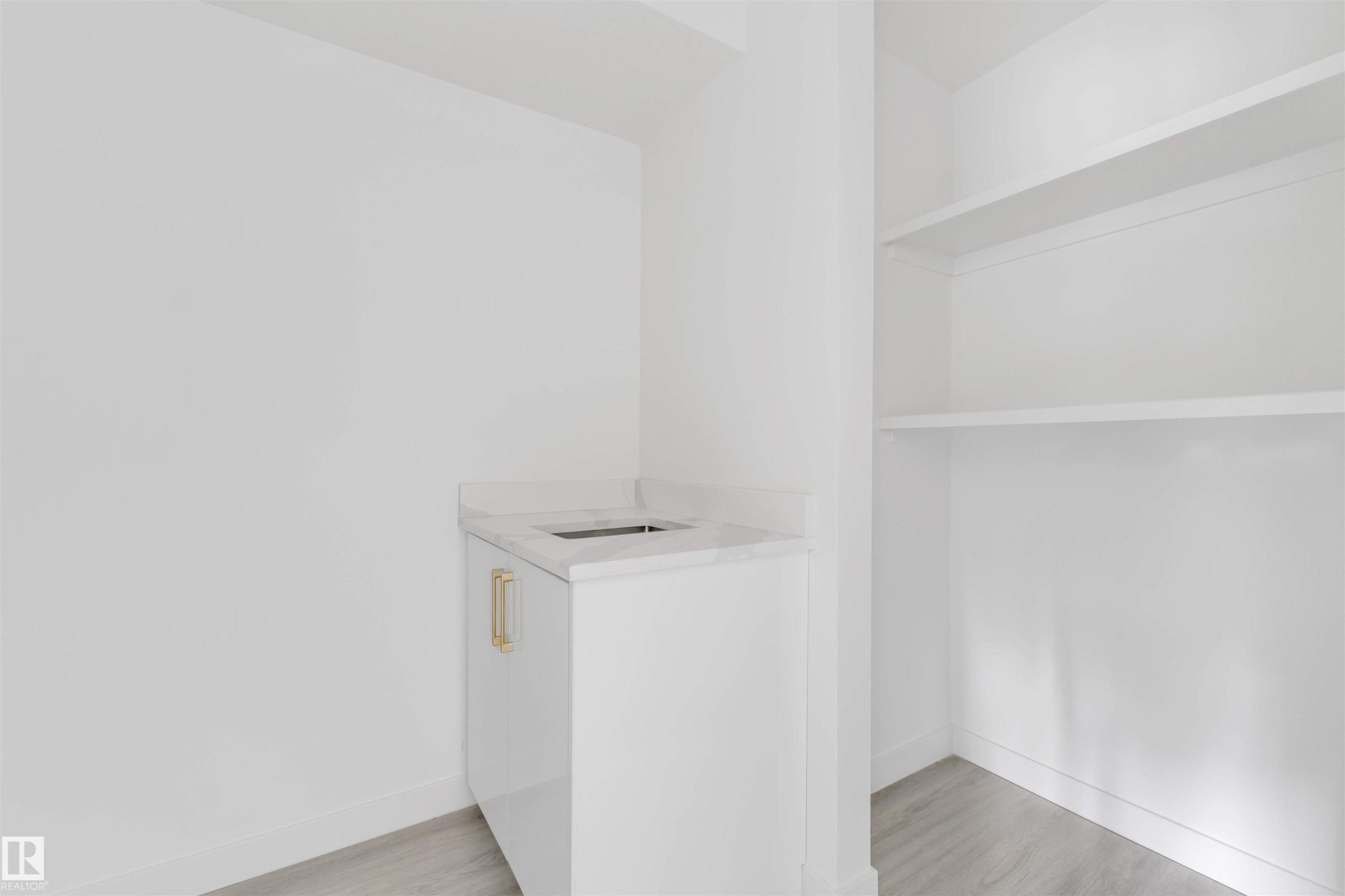 Compact wet bar featuring a white cabinet with gold-toned hardware, an integrated sink, and a stone-finish countertop - 3605 112 Ave, Edmonton, AB