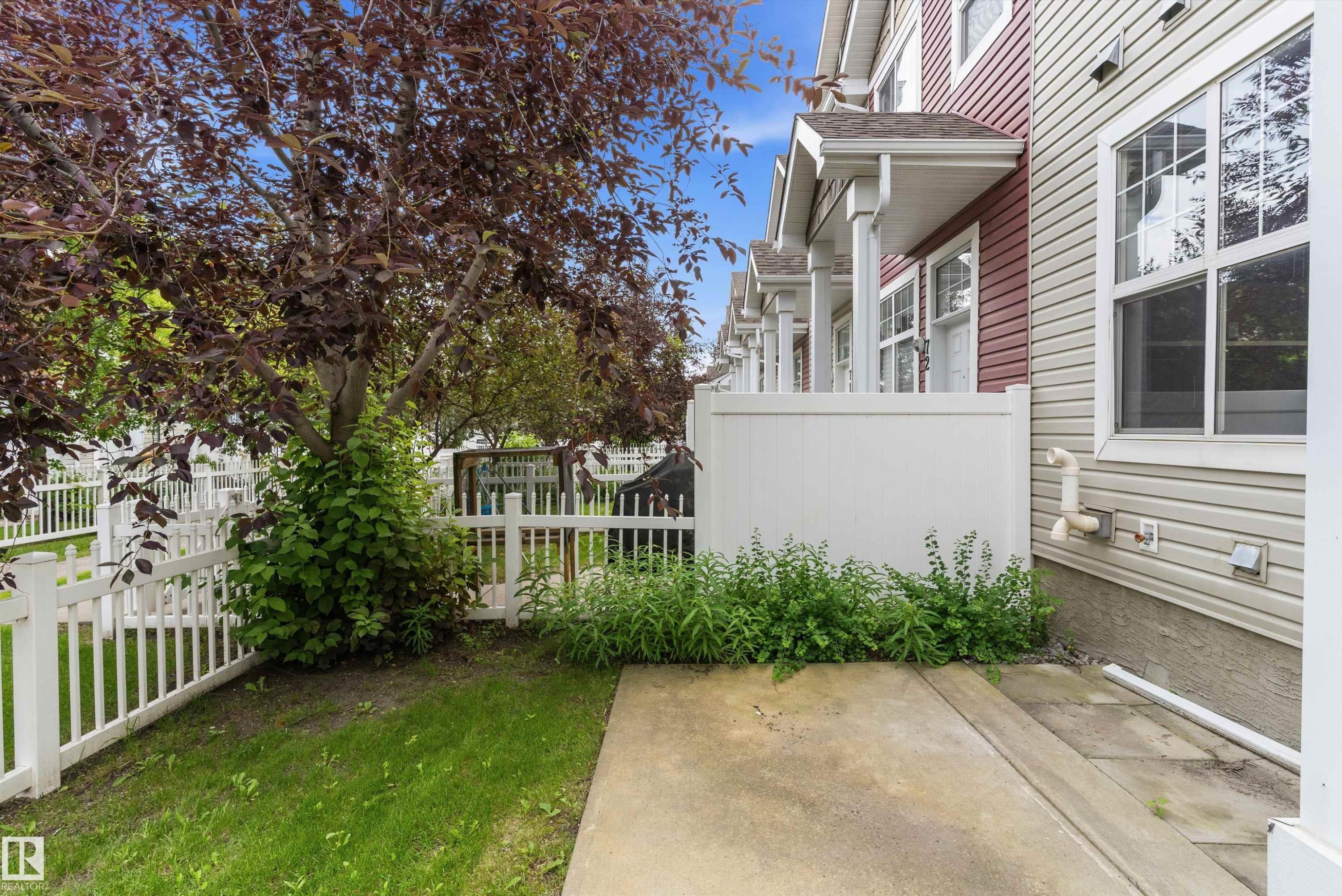 Patio area featuring a mature tree, white picket fencing, and a concrete pad - 73 2051 Towne Centre Boulevard, Edmonton, AB